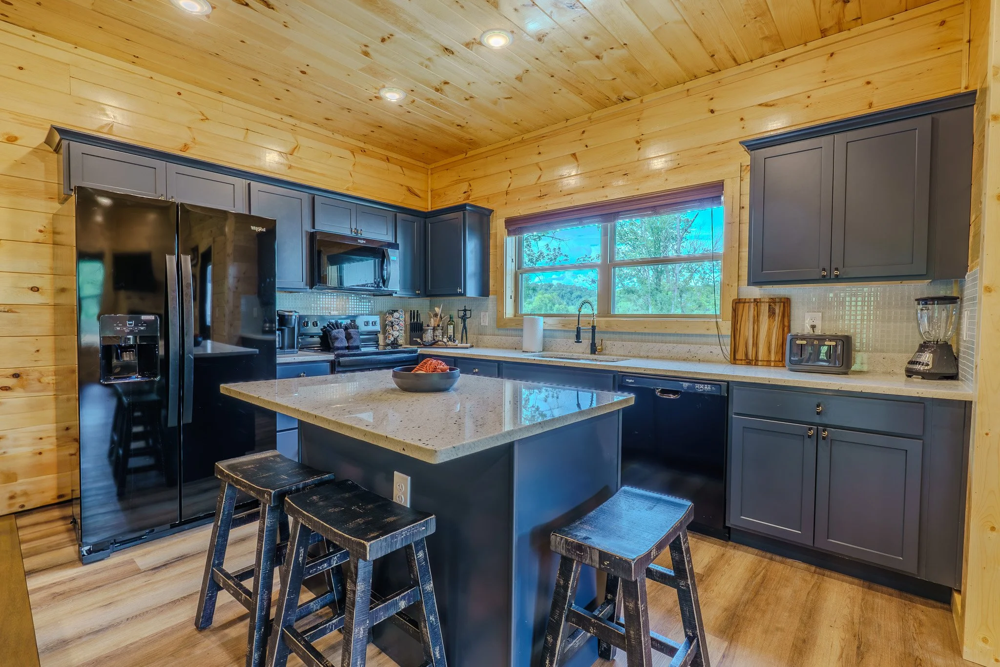 Kitchen with wooden walls and ceiling, black appliances, gray cabinets, a kitchen island with stools, window with scenic view.