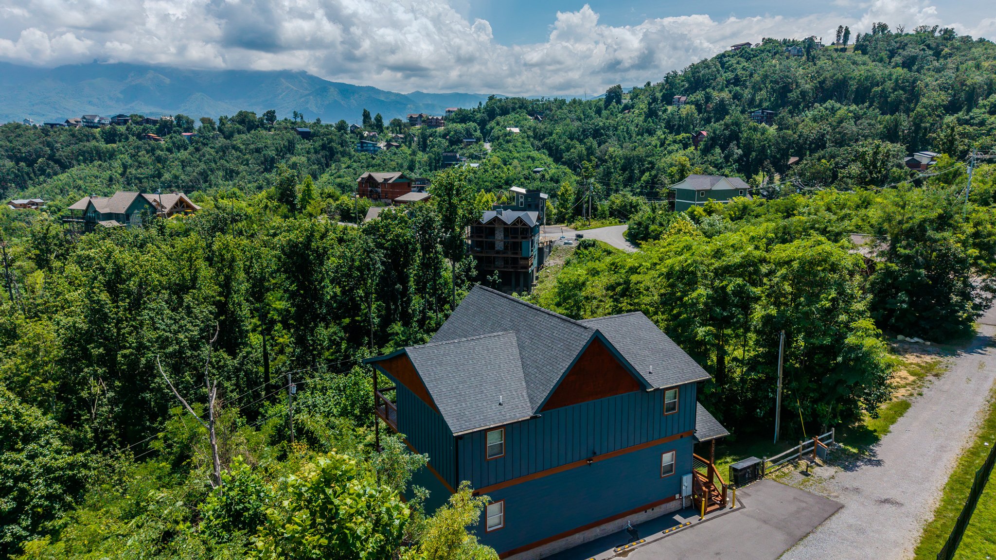 A scenic view of a mountainous, forested area with residential houses scattered on the hillside and a cloudy sky overhead.