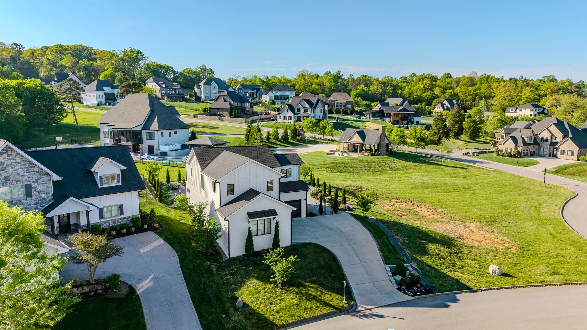 Aerial view of a residential neighborhood with modern houses, green lawns, and trees on a sunny day.