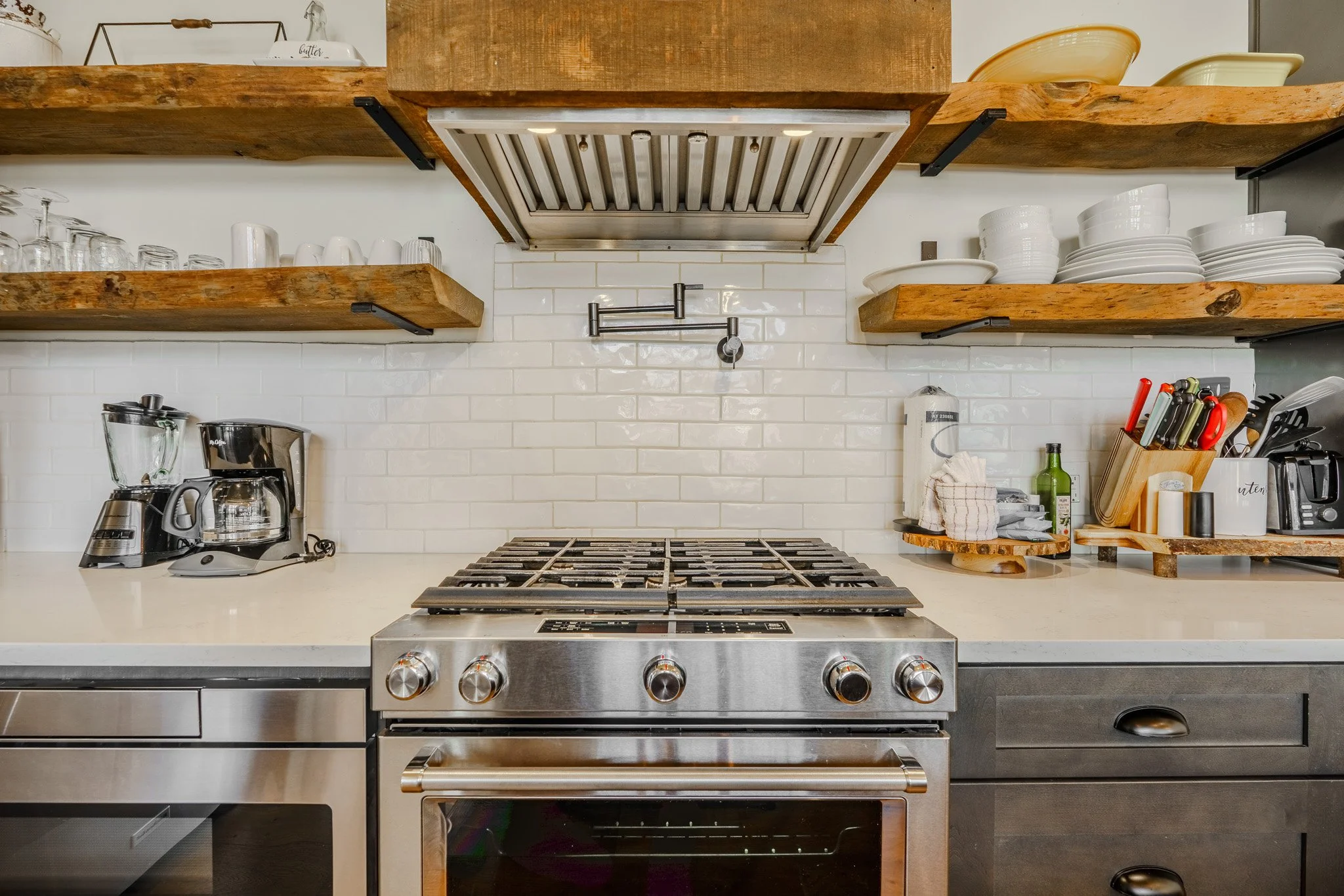 Kitchen stove with wooden shelves holding dishes and utensils above a white countertop with small appliances and accessories.
