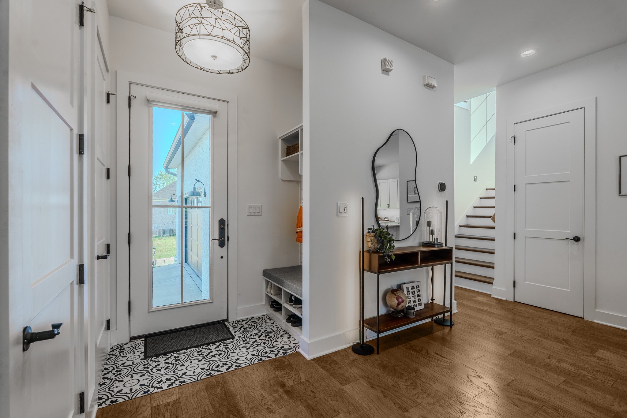 Entryway with a glass door leading outside, a patterned rug, a wooden console table with decorative items, and a staircase in the background.