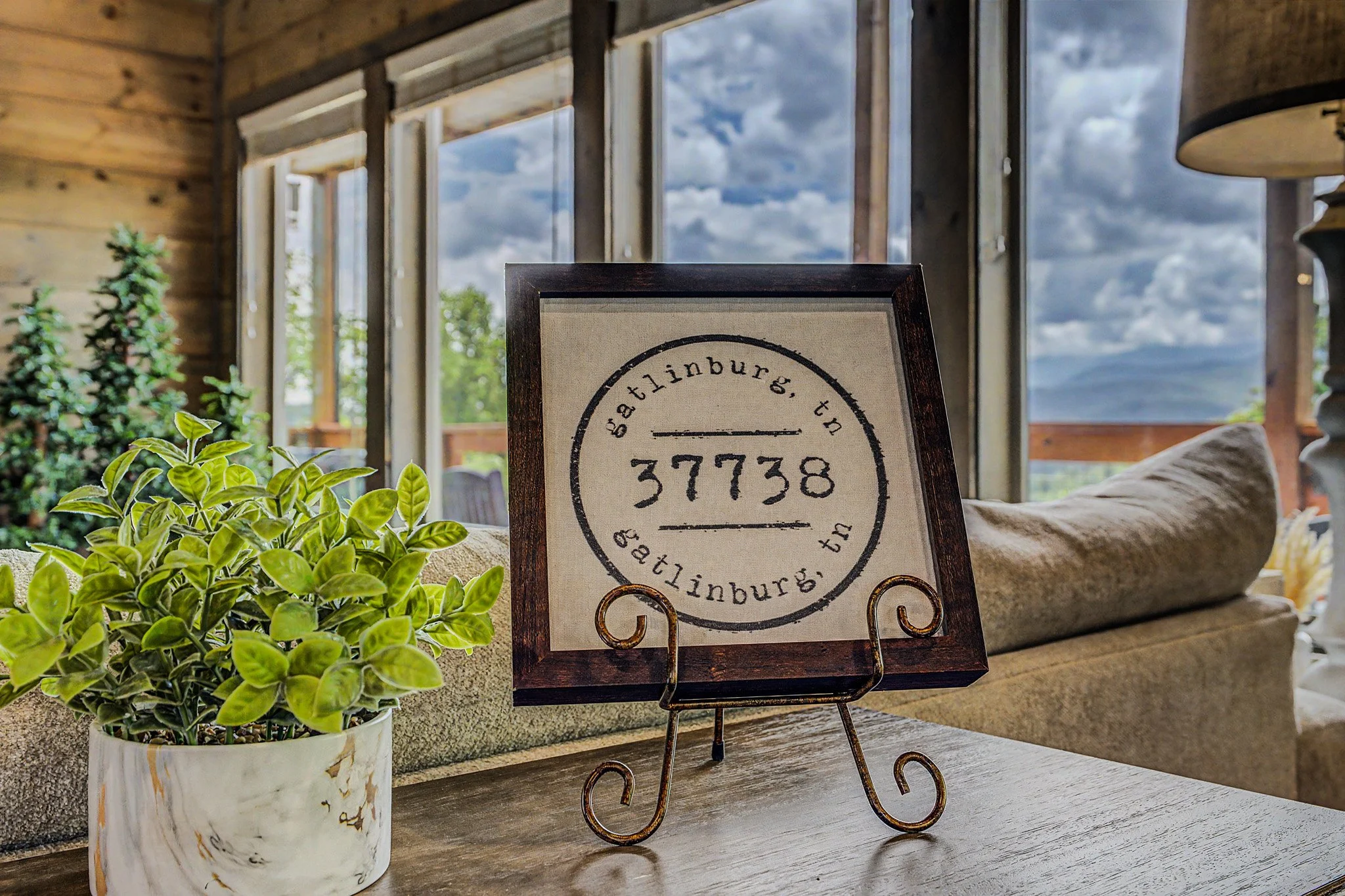 Potted green plant, framed sign with text, in a room with large windows and cloudy sky outside.