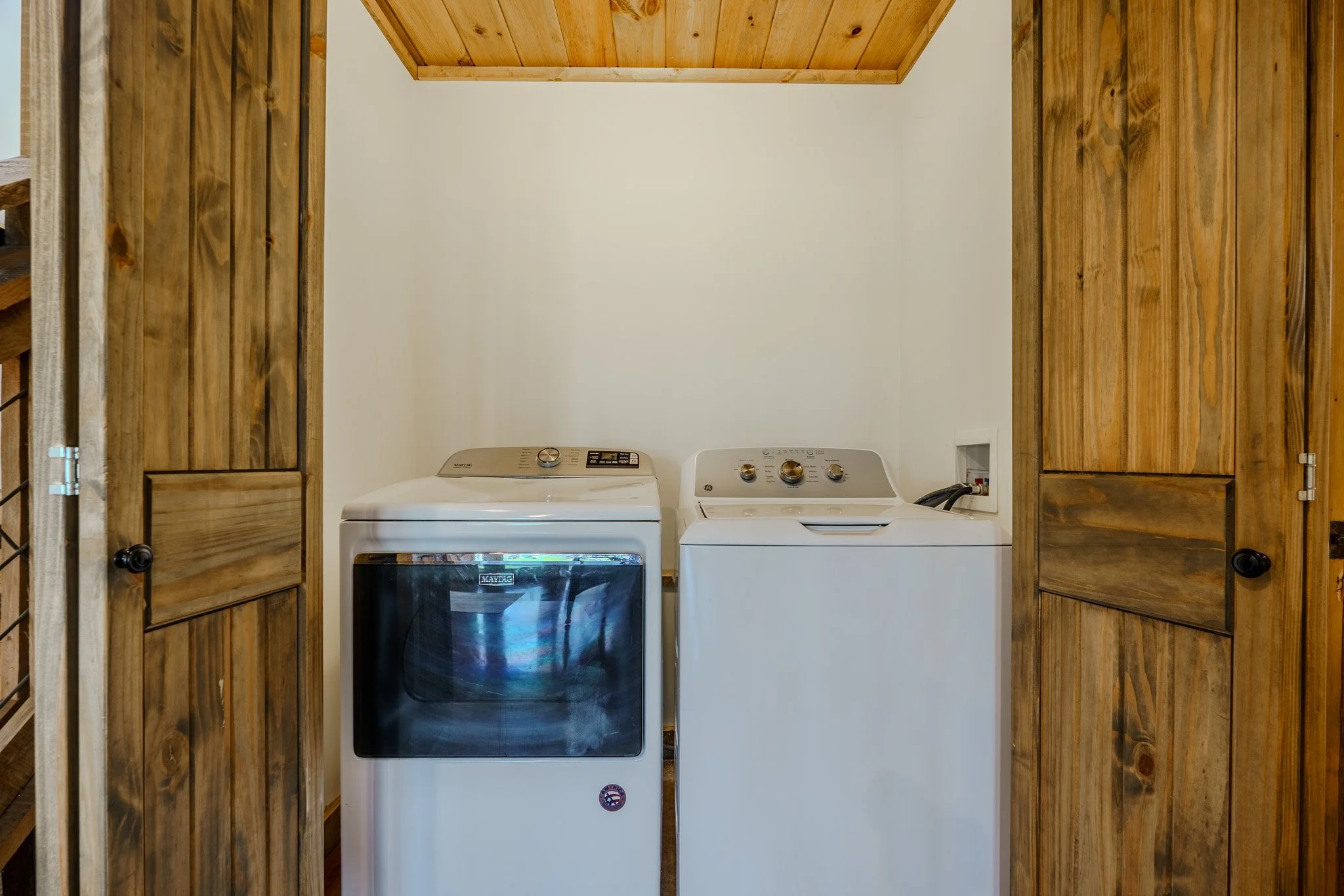 Laundry room with wooden sliding doors, containing a white washing machine and a white dryer side by side against a white wall.