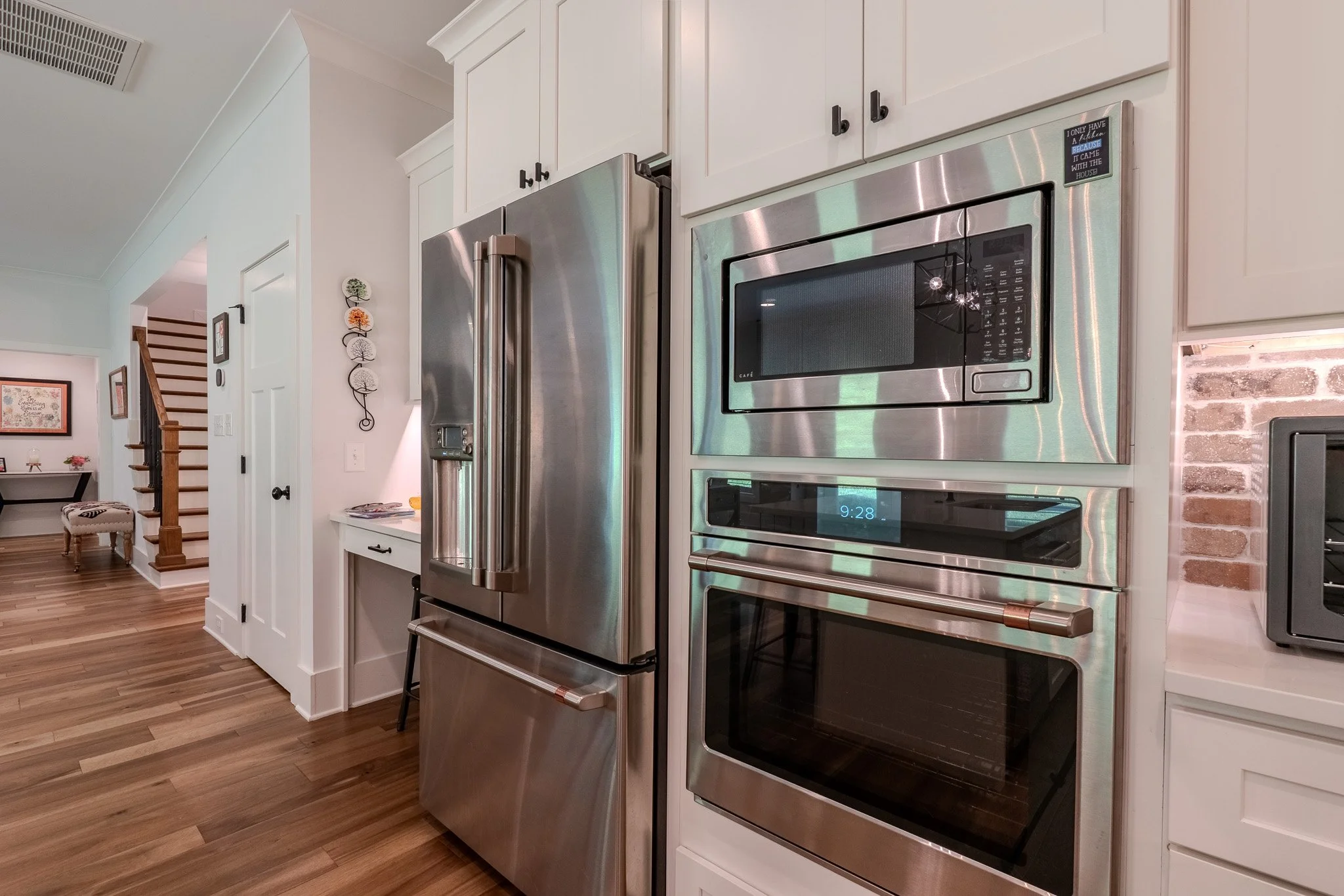Stainless steel refrigerator, microwave, and oven built into white kitchen cabinetry with hardwood floors.