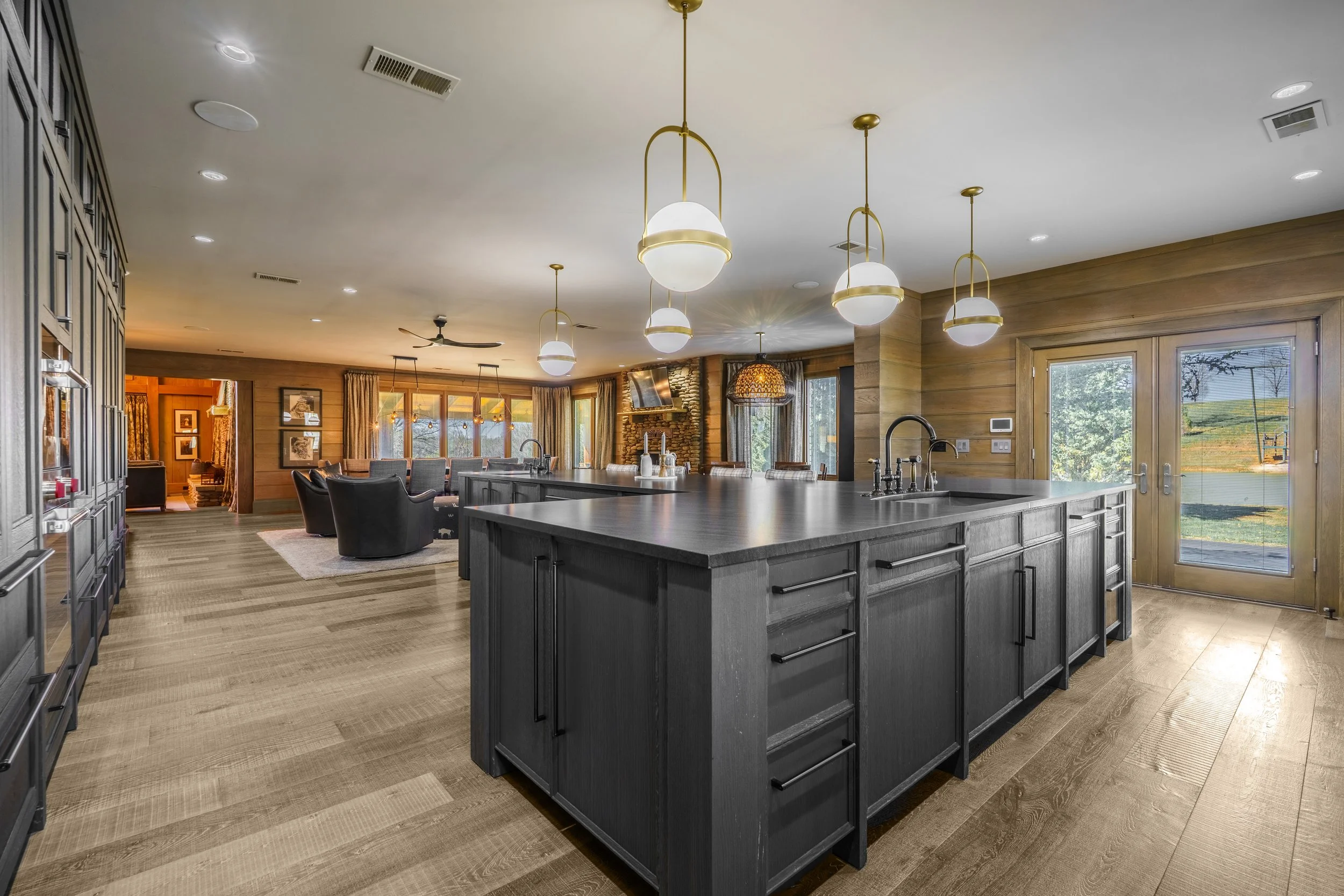 Modern kitchen with black island, hardwood flooring, pendant lighting, and adjacent living area with seating and fireplace.