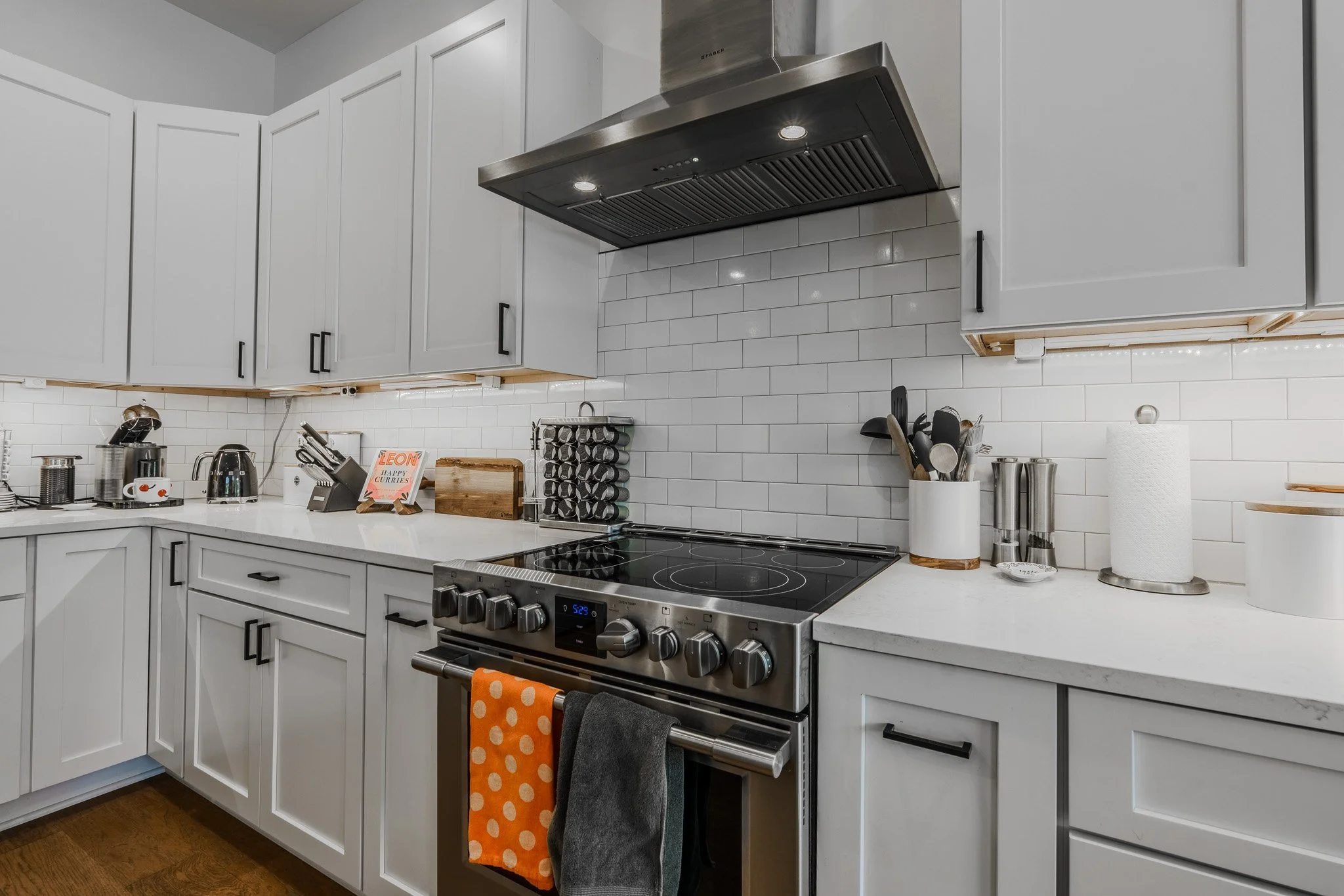 Modern kitchen with white cabinetry, stainless steel stove and range hood, white subway tile backsplash, and countertop appliances.