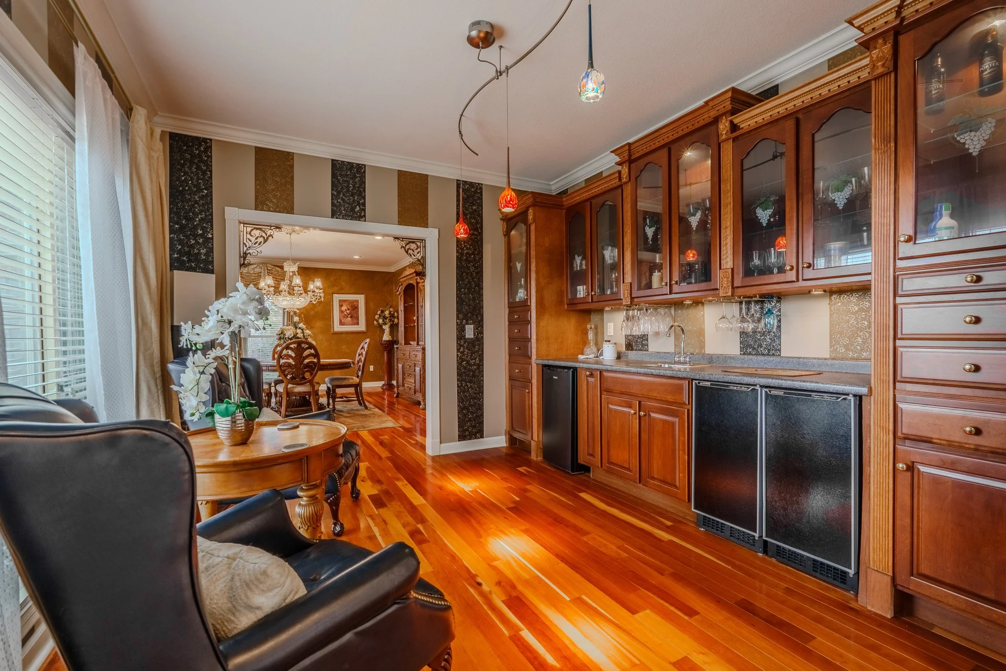 Spacious kitchen with wooden cabinets, a granite countertop, and hardwood floors, with a view into a dining room with a chandelier and wooden dining table.