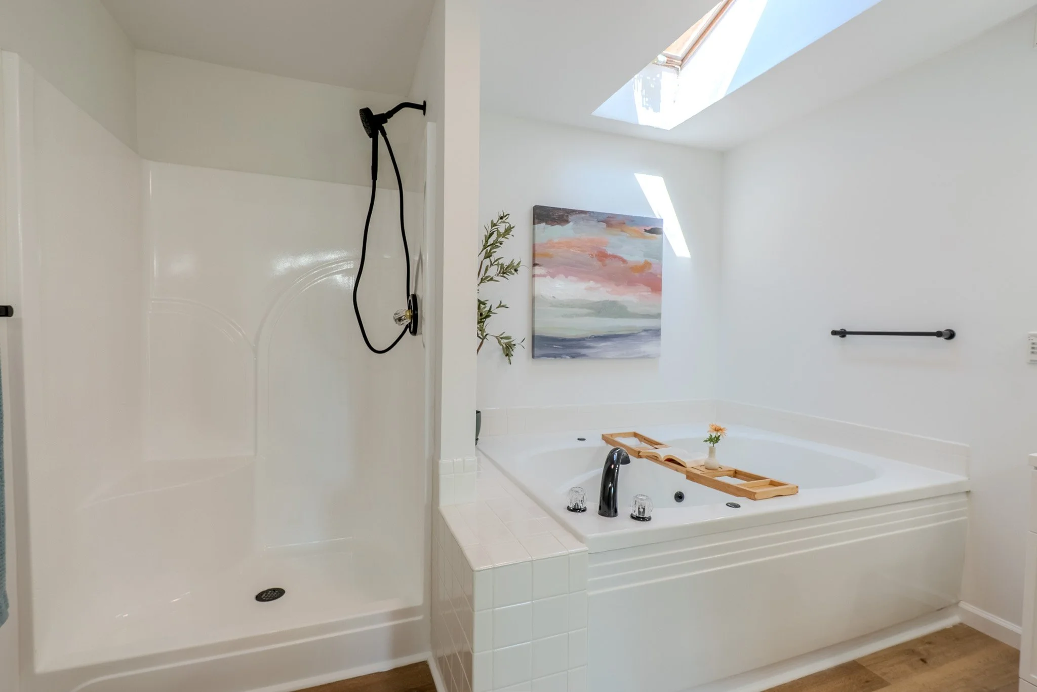 Bathroom with a shower area on the left and a bathtub on the right, featuring a skylight, art painting, and a towel rack.