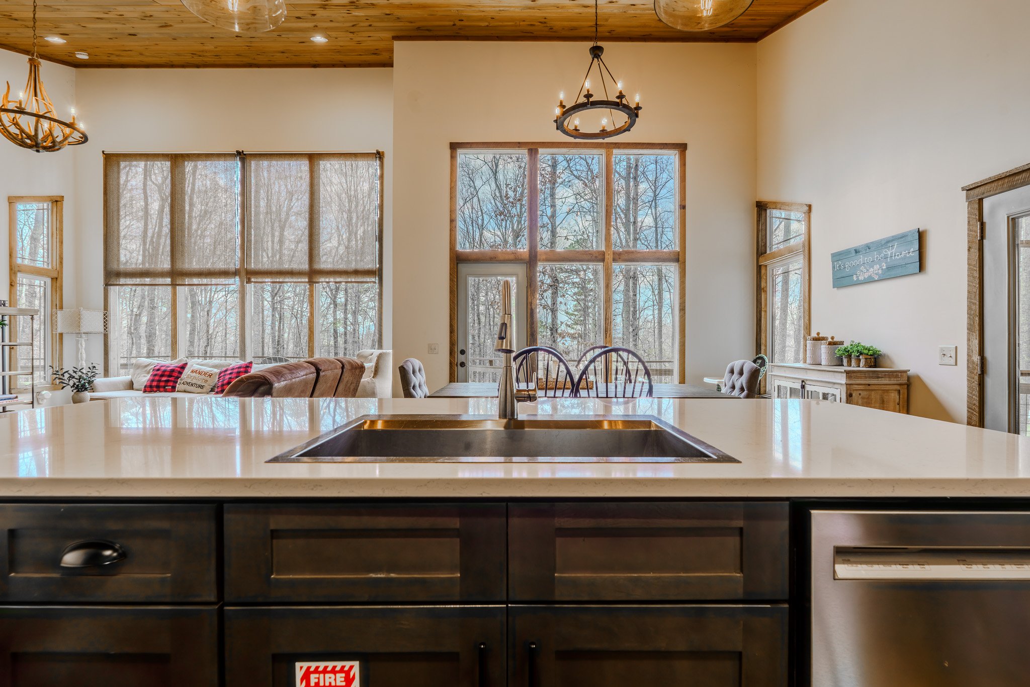 Open-concept kitchen with a large granite island, dark wood cabinets, and a view of a living area with a sofa, windows, and trees outside.