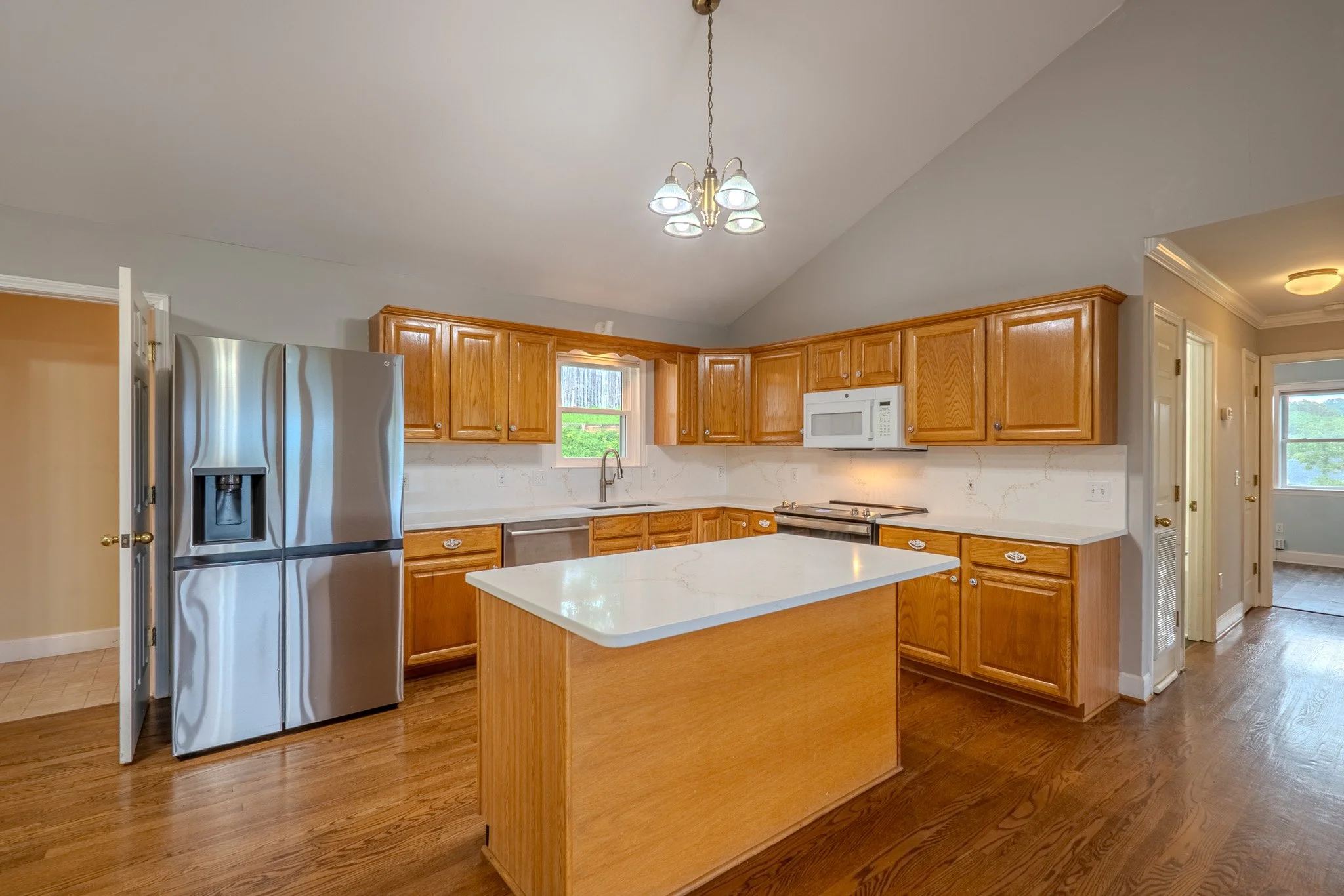 Kitchen with wooden cabinets, white marble countertops, stainless steel refrigerator, microwave, and wooden flooring.