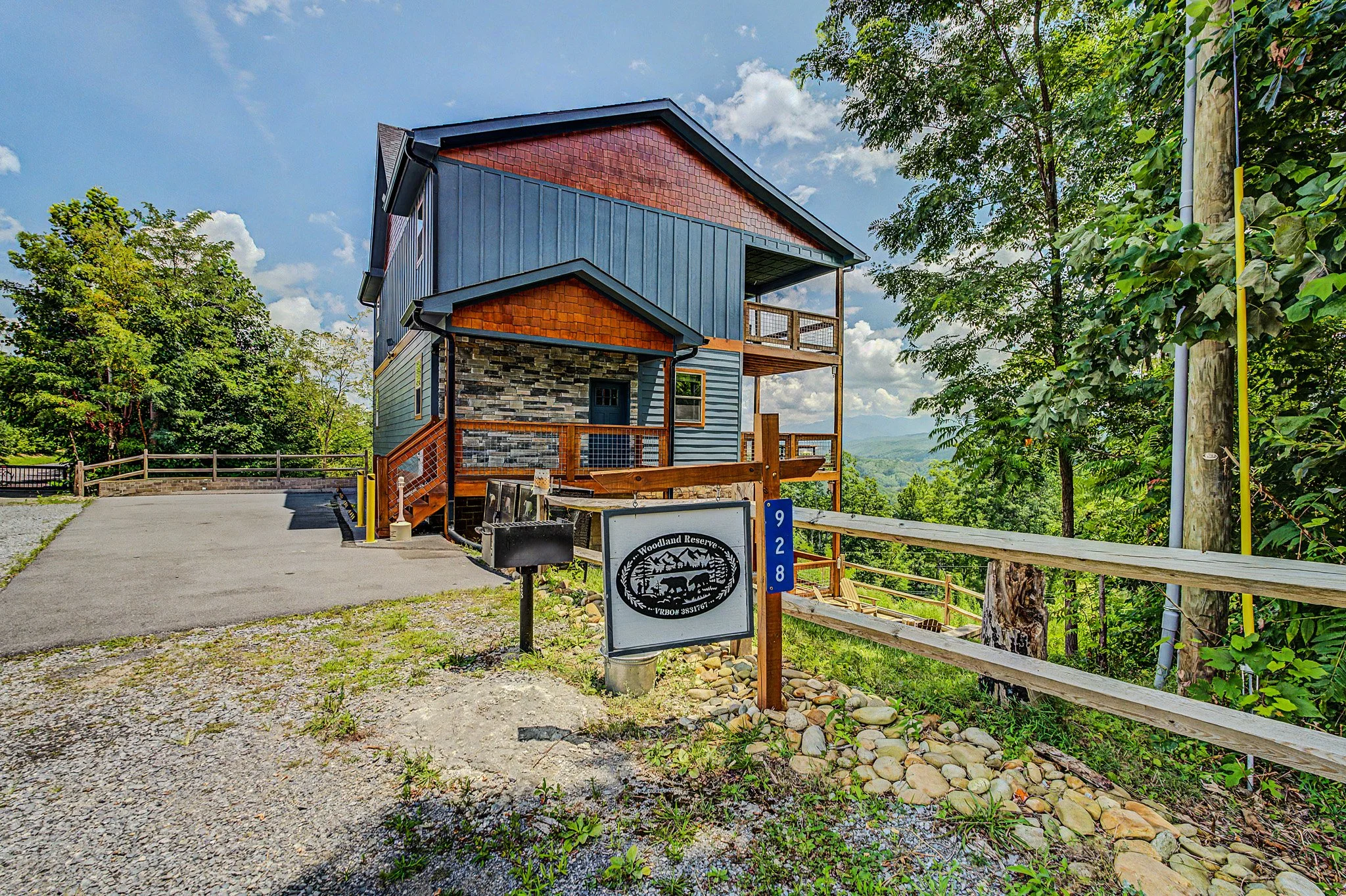 Colorful modern house with blue siding and red accents, surrounded by trees, with a pathway and a sign for Woodland Reserve.