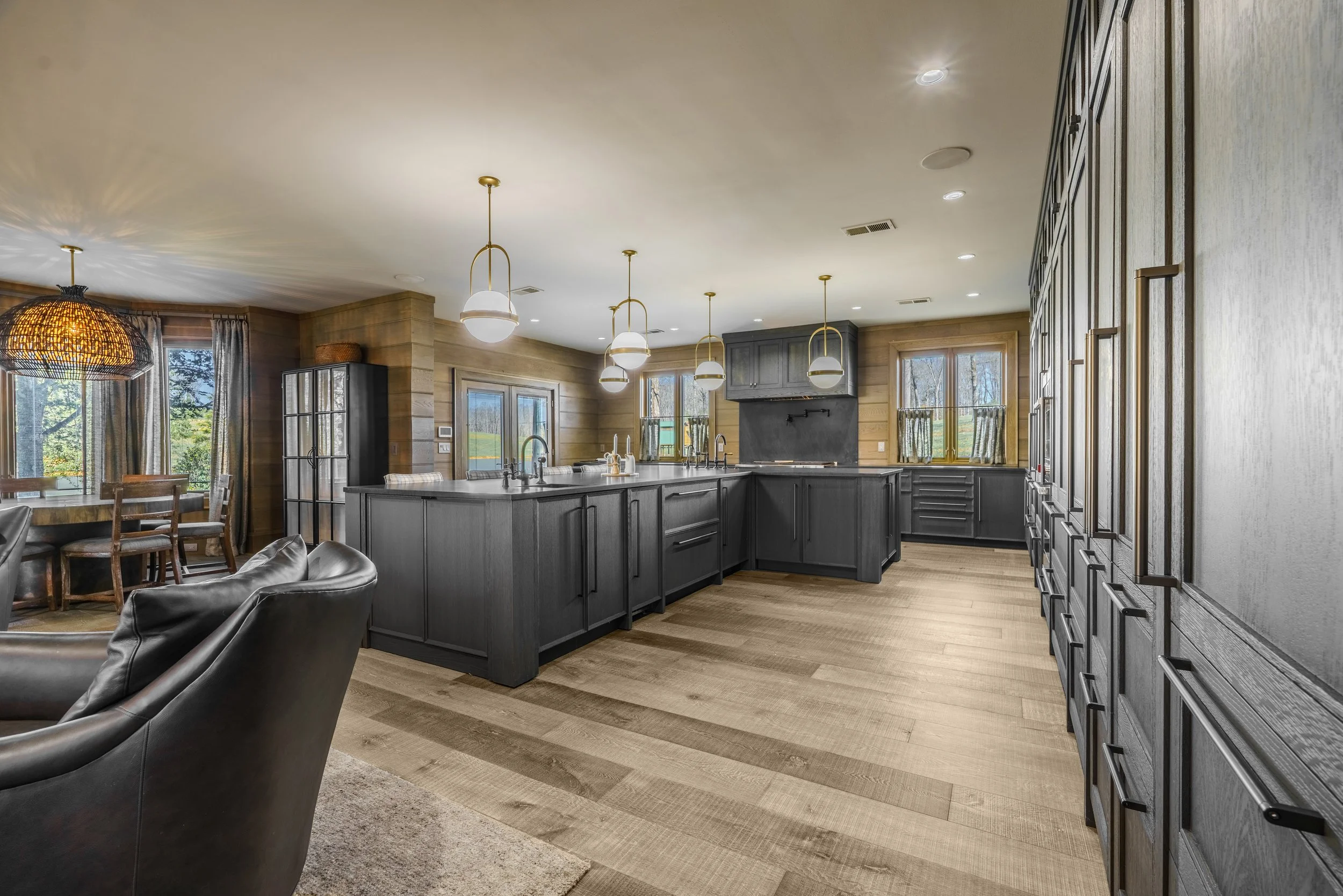 Modern kitchen with black cabinets, island, and pendant lighting, surrounded by wooden walls and flooring.