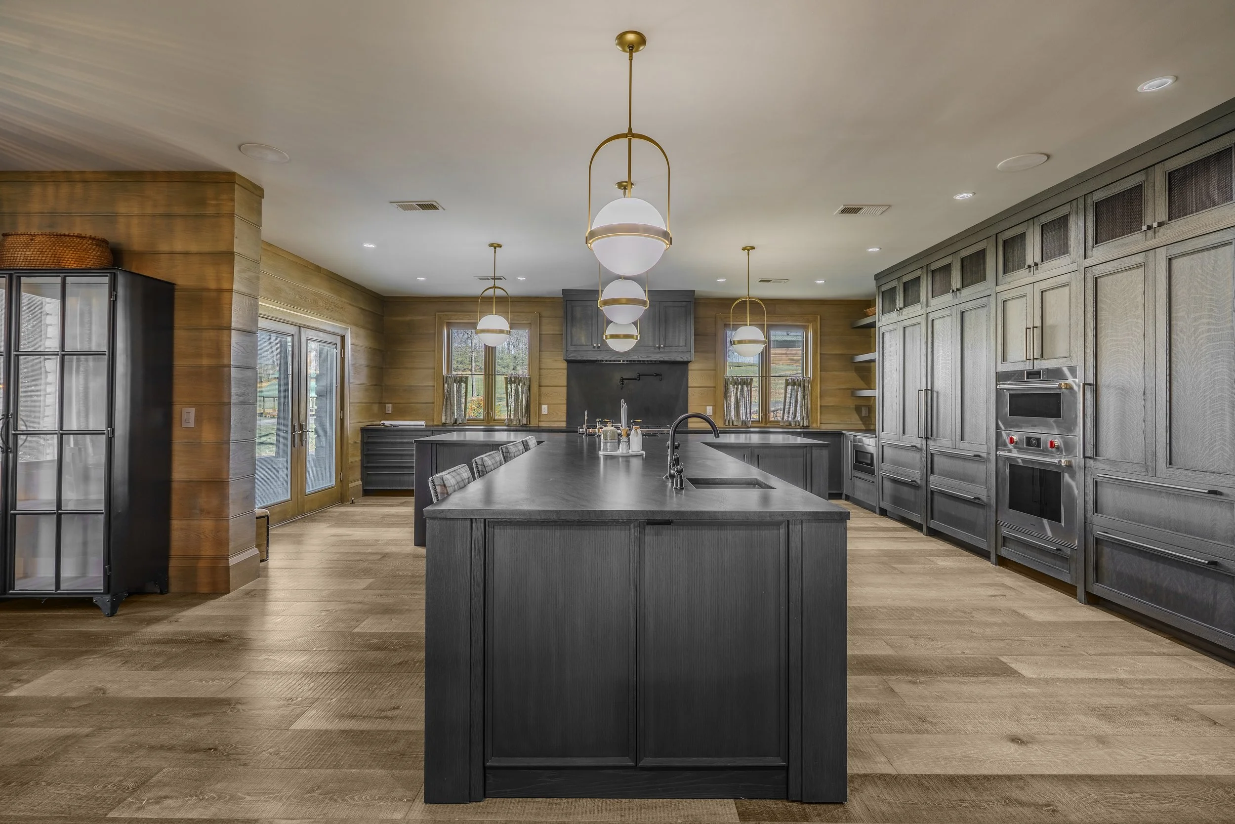 Modern kitchen with dark cabinetry, large island, grey cabinets on walls, wood floors, and pendant lighting.