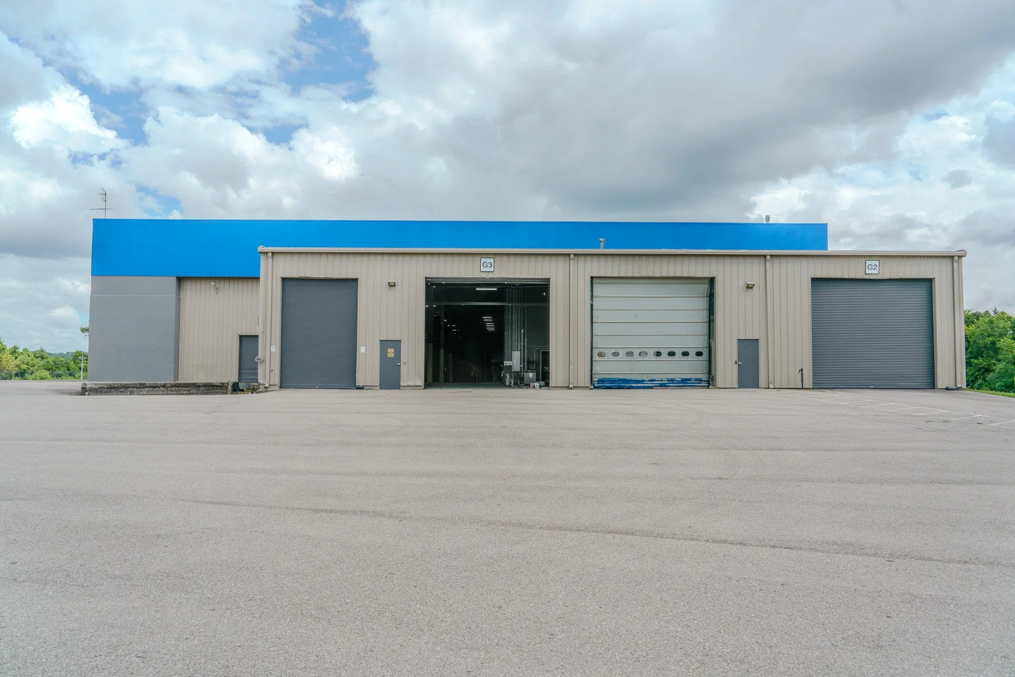 An industrial warehouse building with three large garage doors and a clear sky with some clouds.