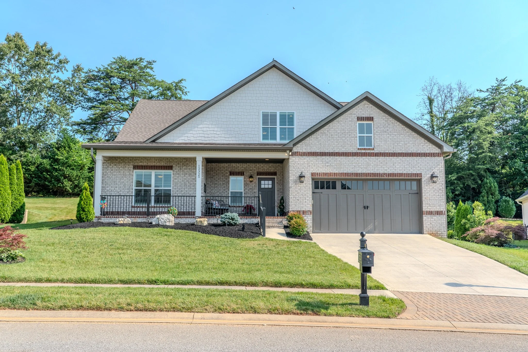 Two-story modern house with a brick and siding exterior, attached garage, well-maintained lawn, and landscaping, on a sunny day.