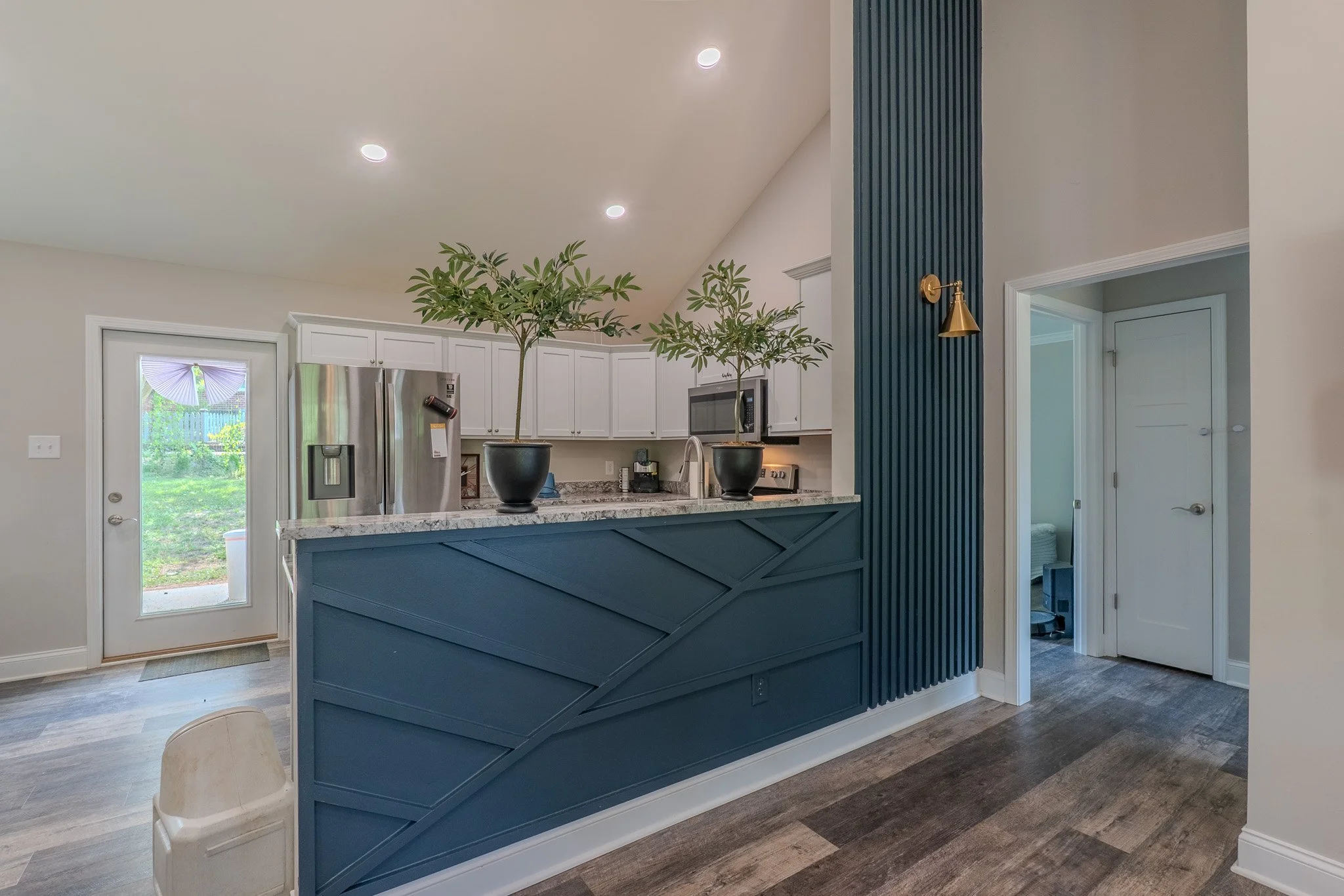 Modern kitchen with white cabinets, stainless steel appliances, granite countertops, and a blue decorative half-wall. There are two potted plants on the counter and a door leading outside.