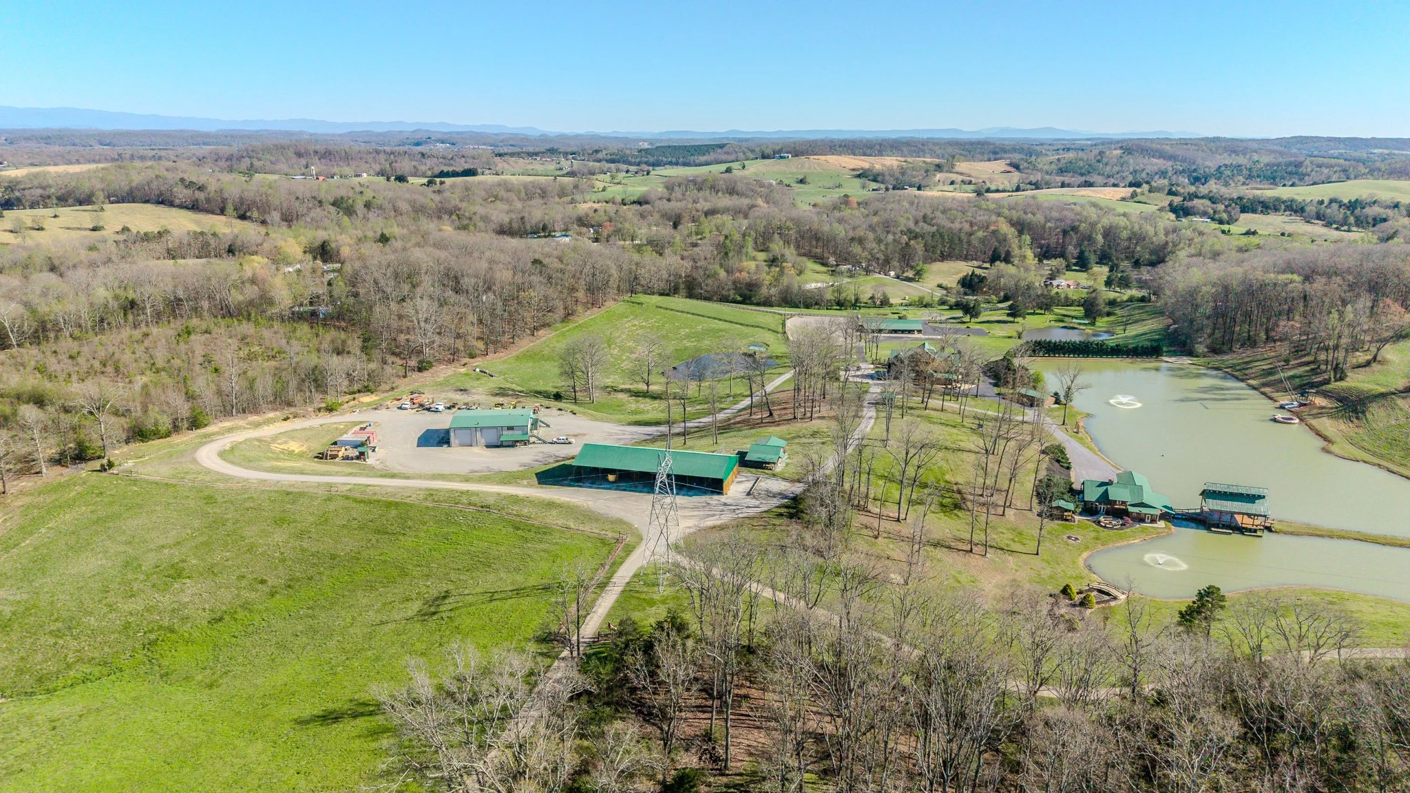 Aerial view of a rural landscape with lakes, green fields, trees, and farm buildings under a blue sky.