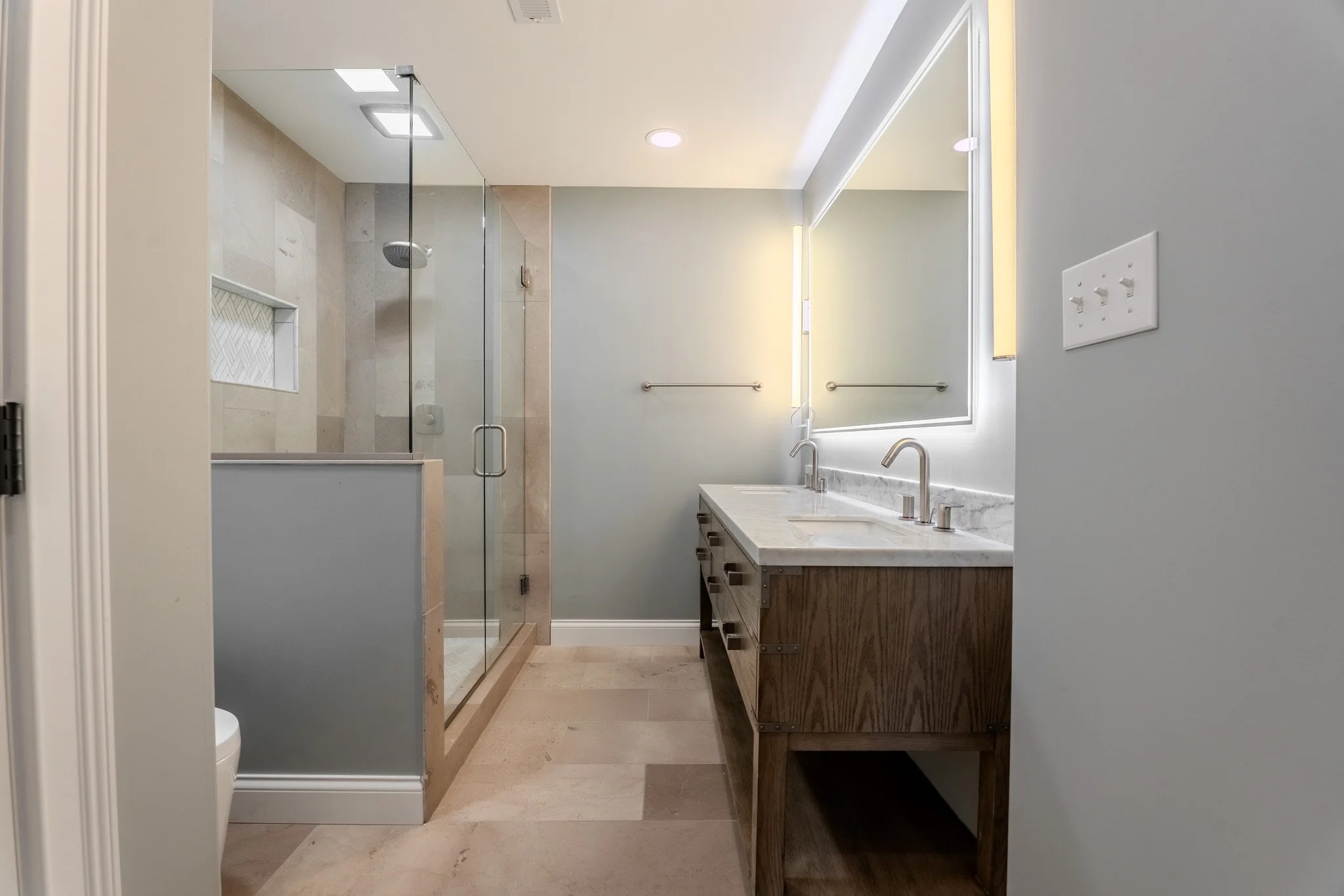 Modern bathroom with a glass shower, double sink vanity with marble top, and a large mirror, in neutral tones.