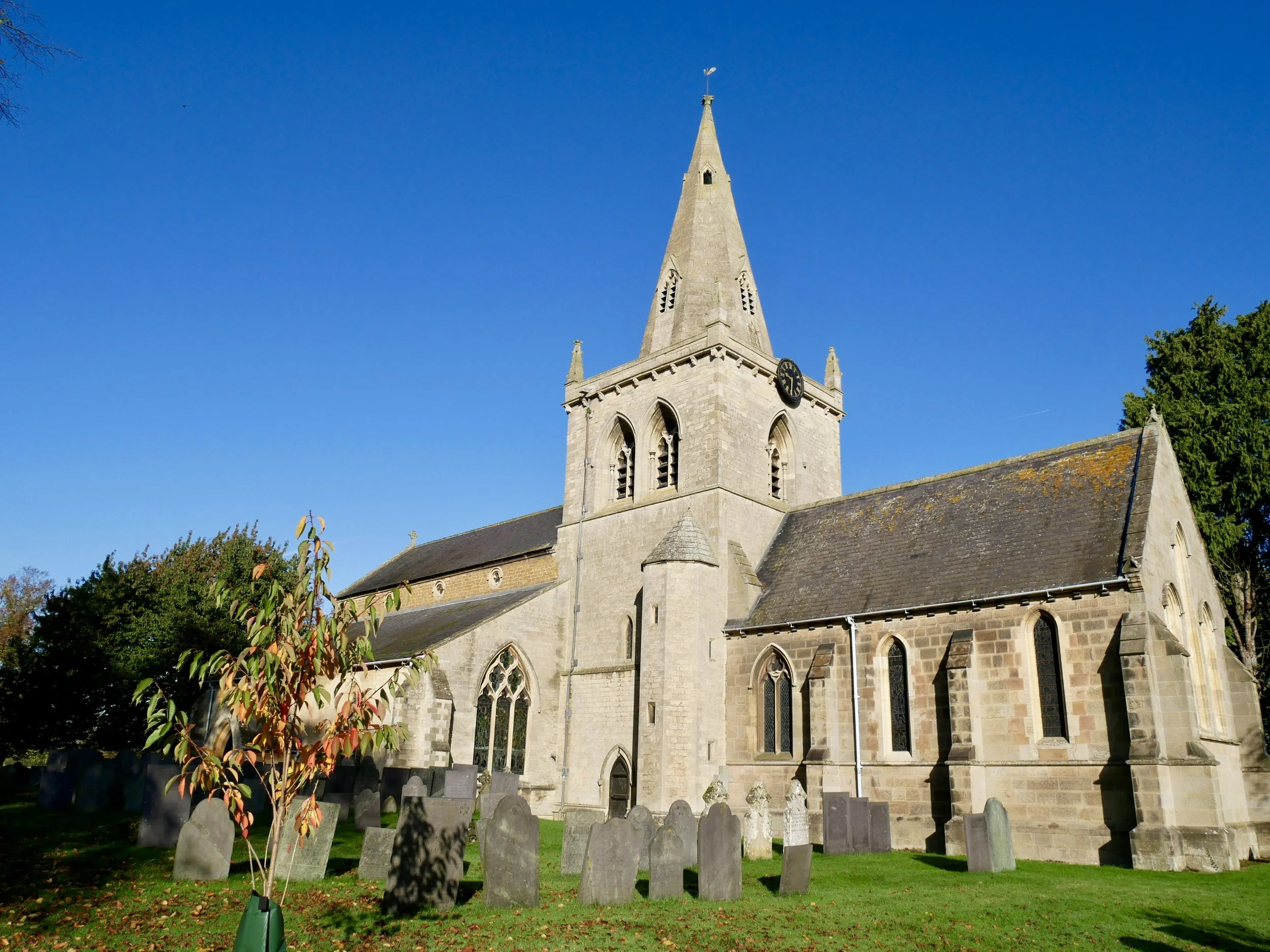 A stone church with a steeple, surrounded by a graveyard with headstones, under a clear blue sky.