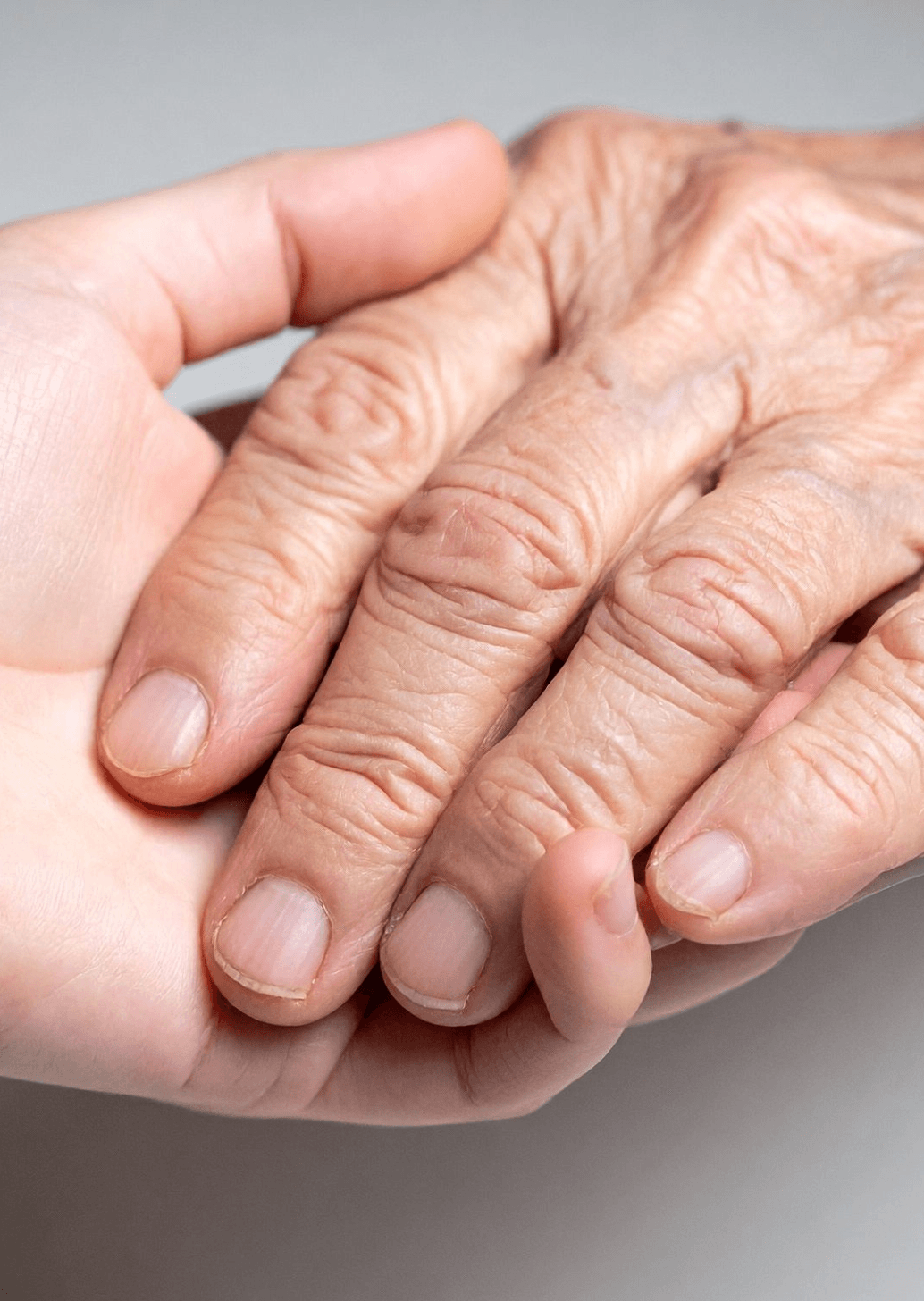 Close-up of an elderly person holding hands with a caregiver, representing support and companionship