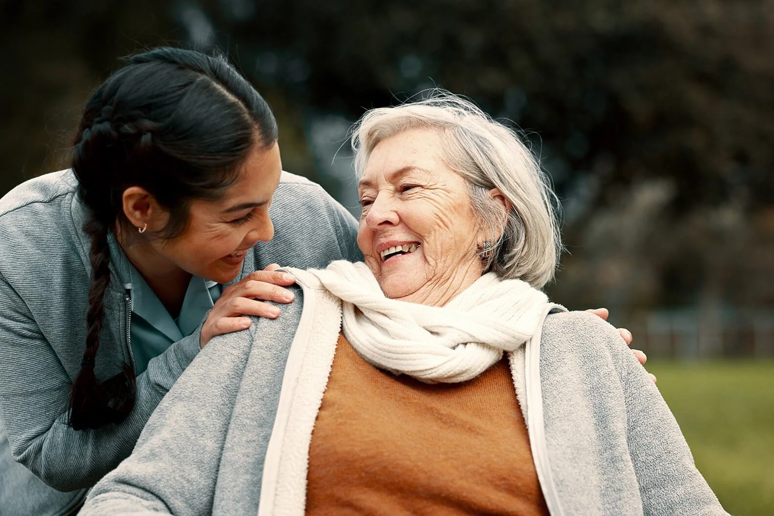 Caregiver sharing a laugh with senior woman outdoors, representing compassionate home and assisted living support.