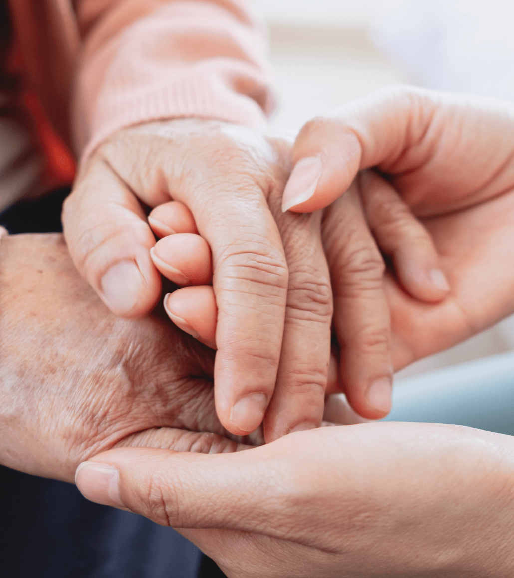 Caregiver gently holding an older adult’s hands to provide comfort and support