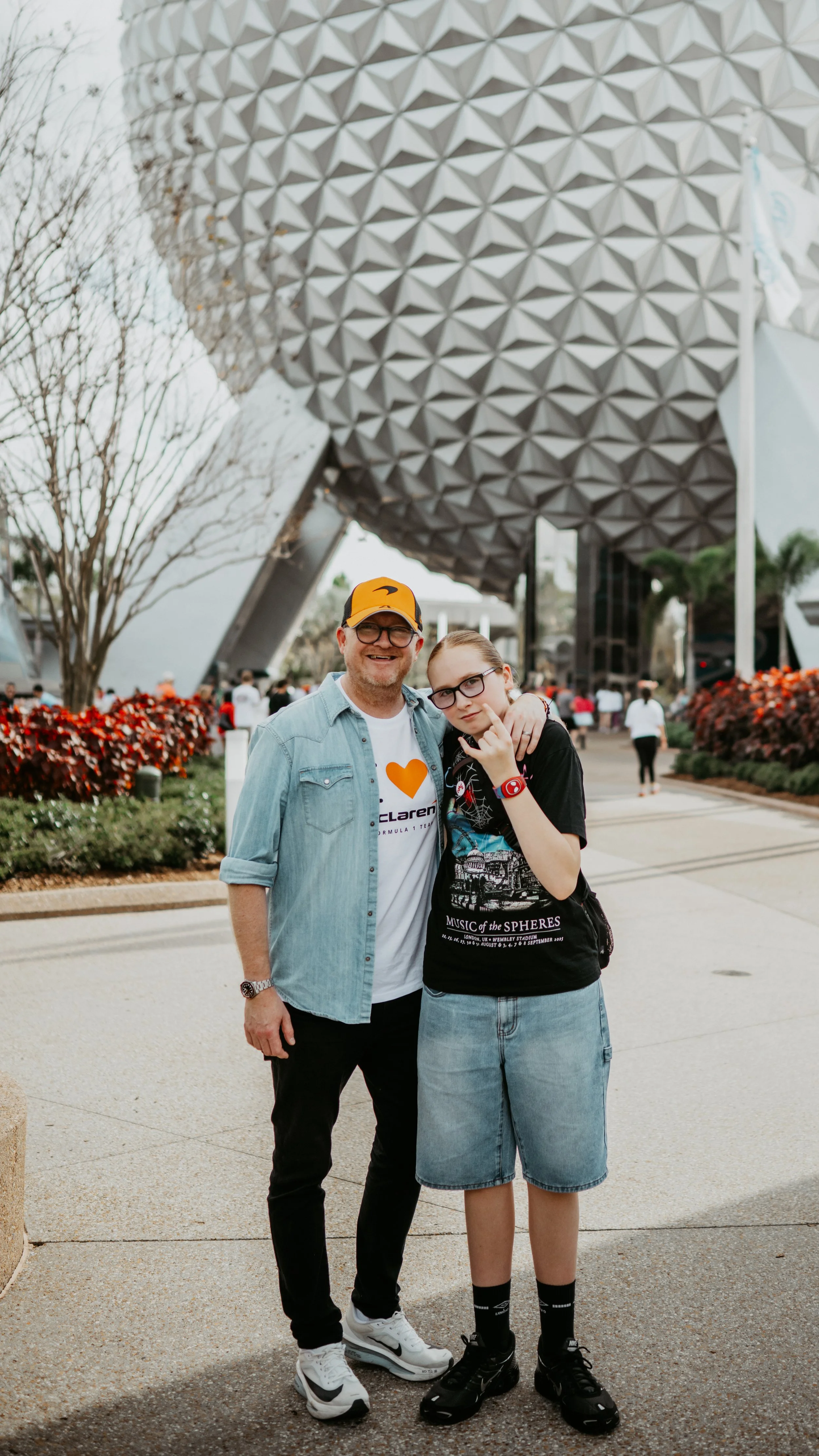 A man and a girl posing together in front of Spaceship Earth at EPCOT, Disney World, with the geodesic sphere in the background.