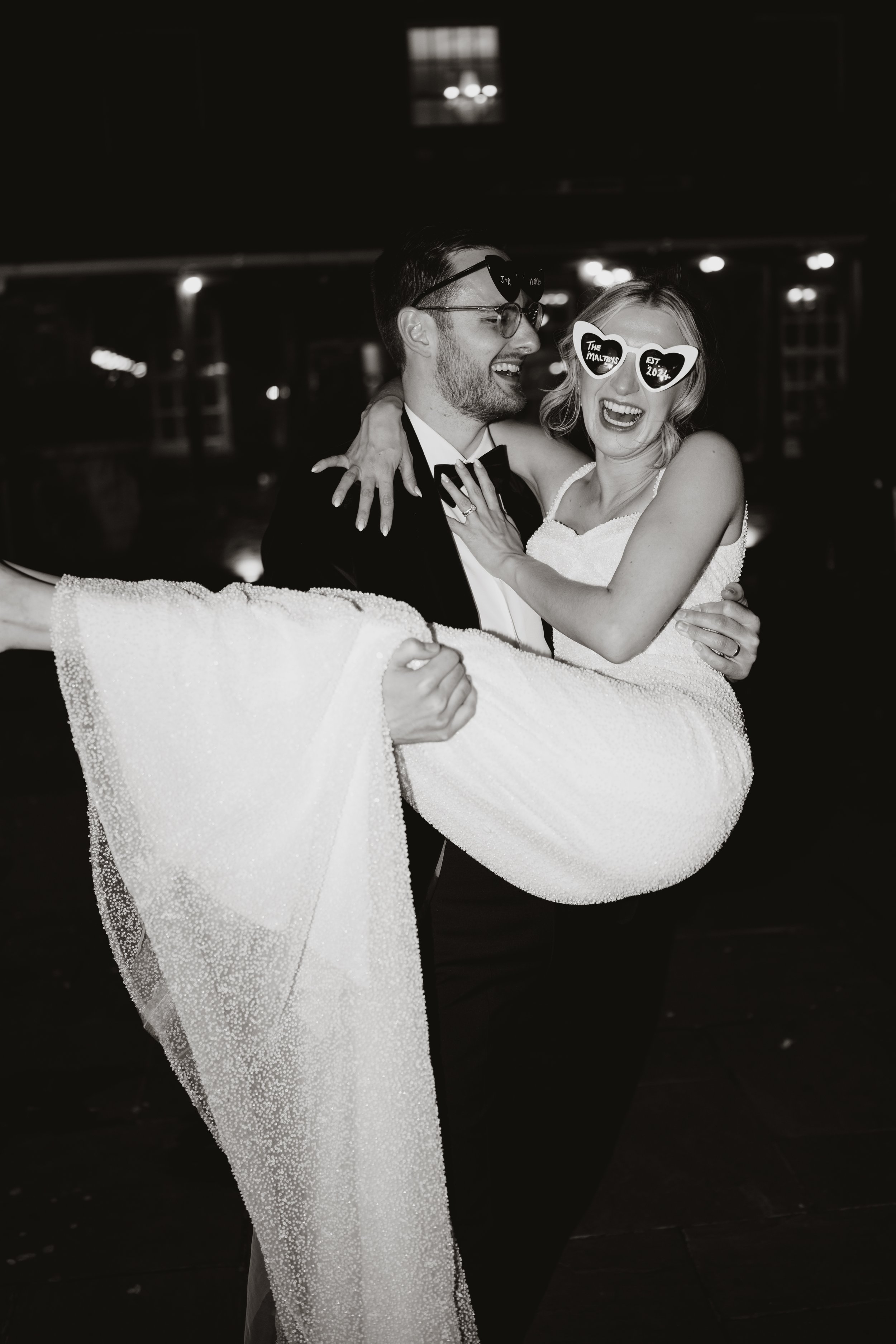 A wedding celebration with a groom and bride happily dancing, with the bride wearing humorous heart-shaped sunglasses that read "The Maltbys" and "Est 2022".