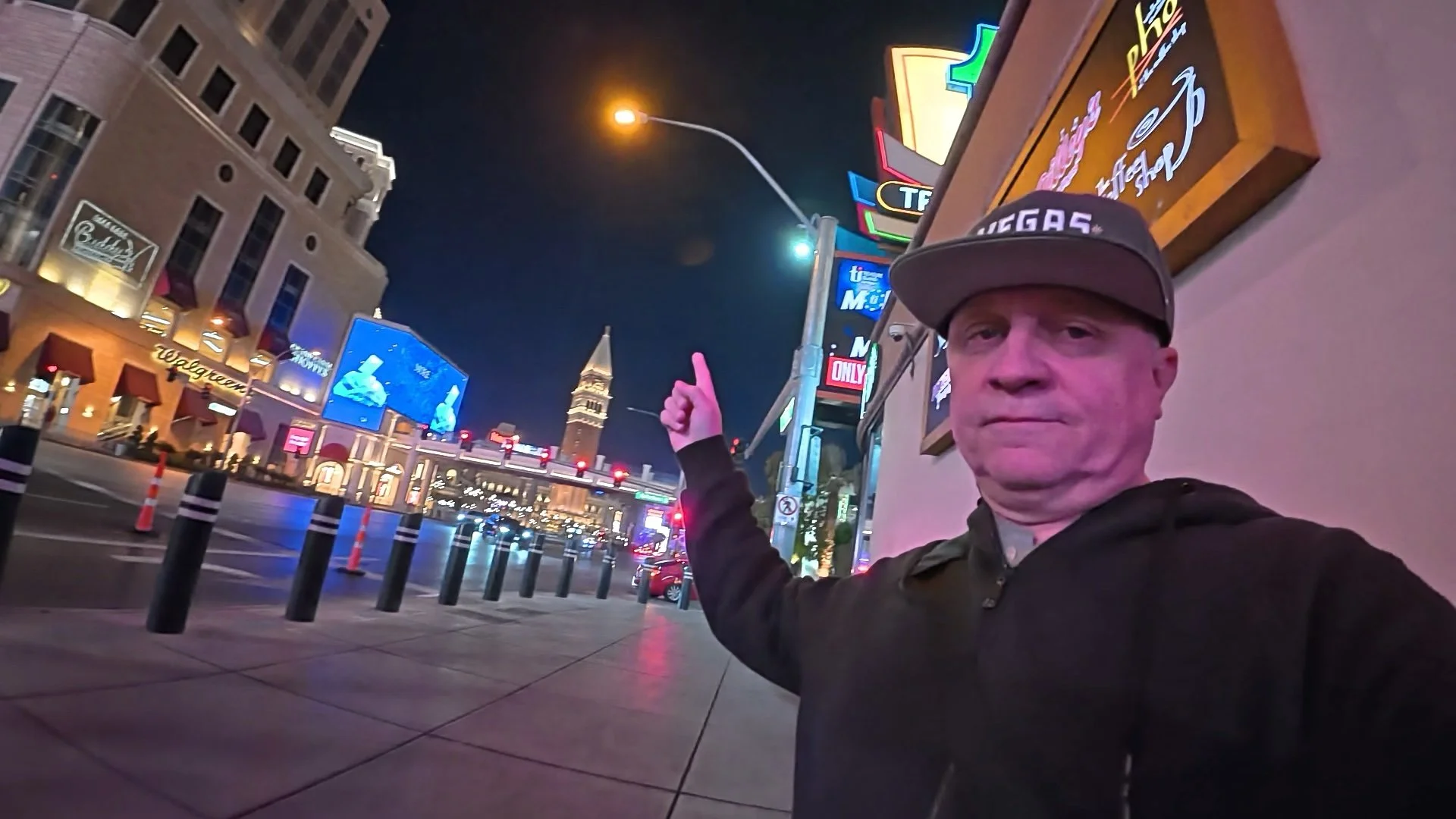 Joel Harris in a video from The Creative Urge, holding a camera, standing outside in an urban area with the Las Vegas Strip in the background.