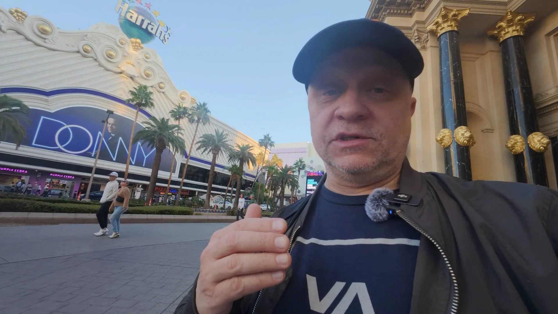 Joel Harris in a video from The Creative Urge, holding a camera, standing outside in an urban area with the Las Vegas Strip in the background.