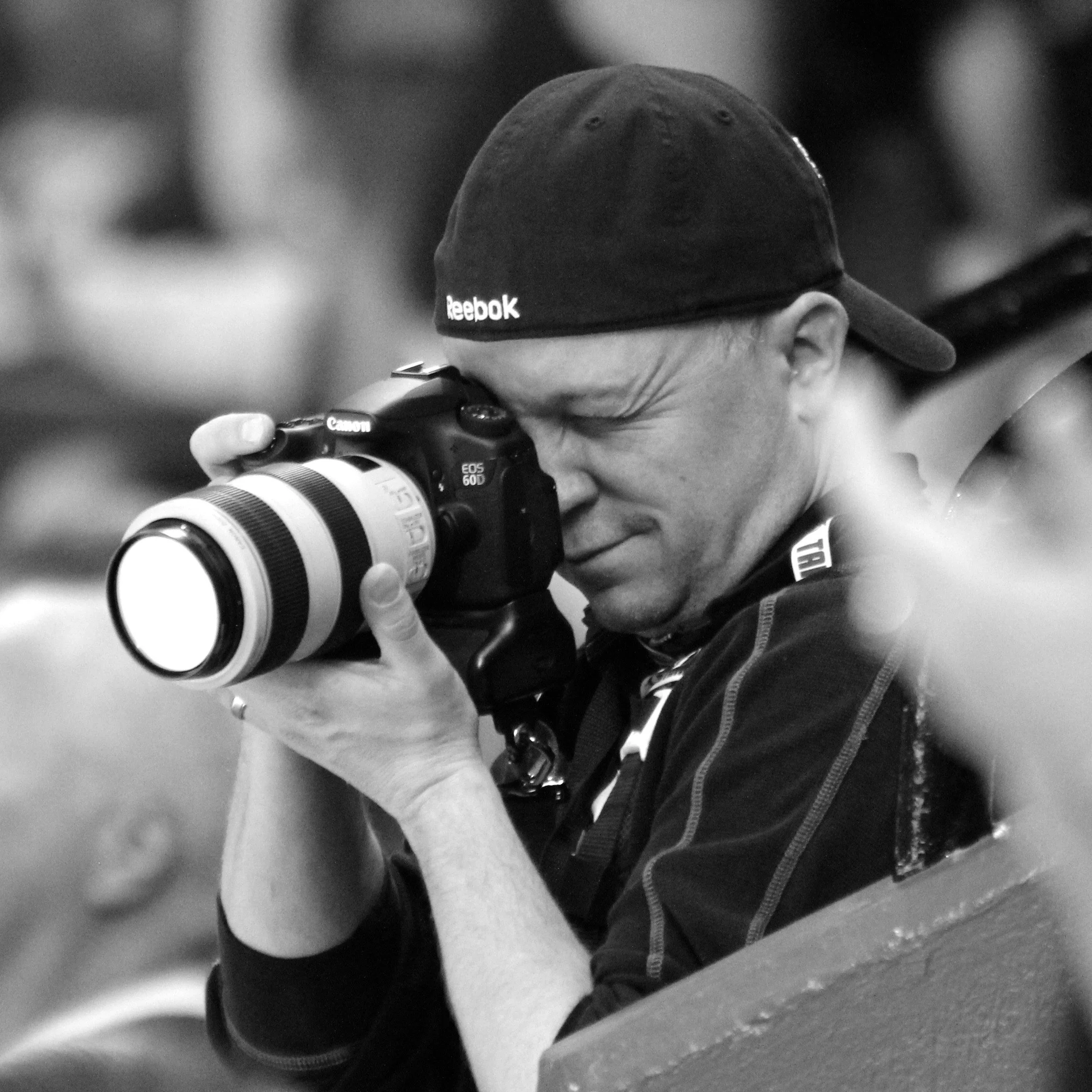 Joel Harris holding a Canon camera, taking a photo in a black and white photo.