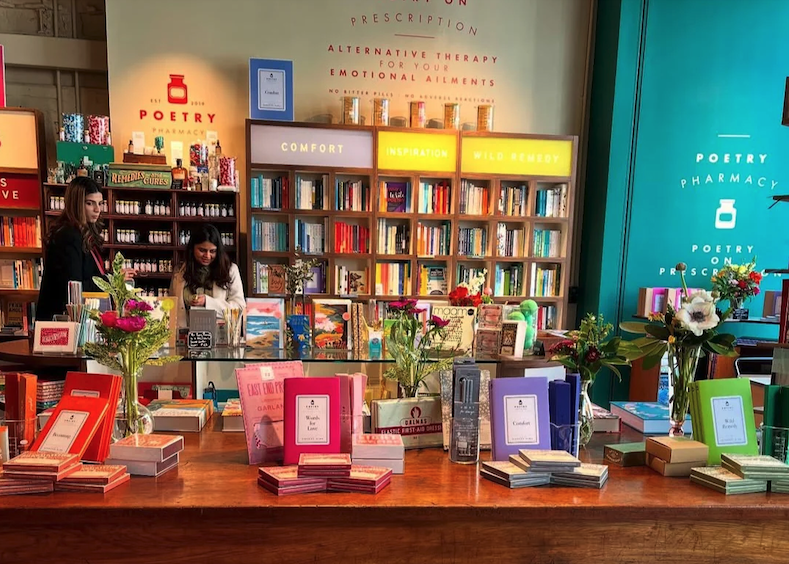 Interior of a bookstore with colorful books and flowers on a wooden table, and shelves filled with books in the background.