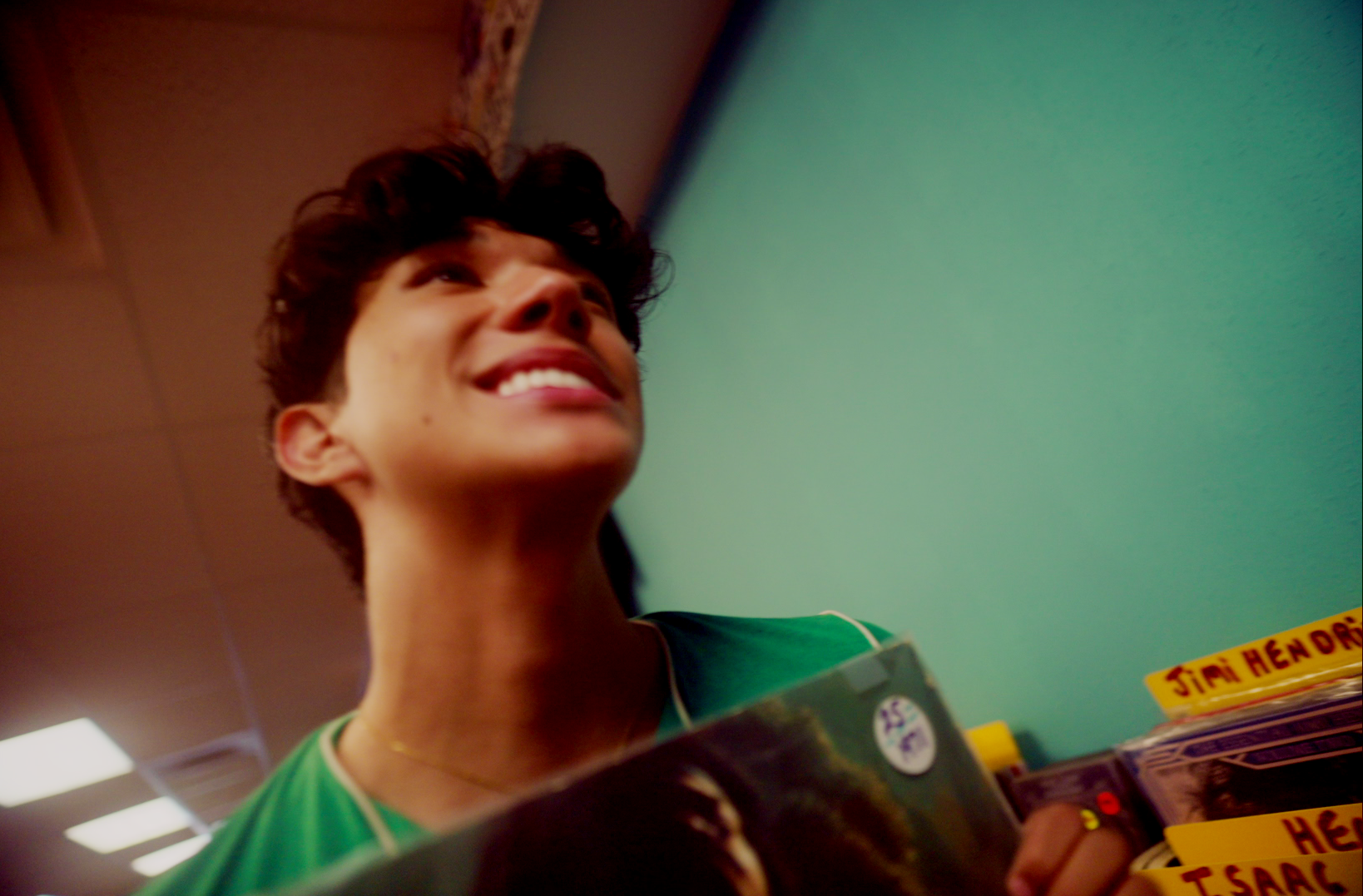 A young man with short, dark hair smiling while shopping at a store, holding a pack of Slim Hendricks cigars with other cigar boxes on display.