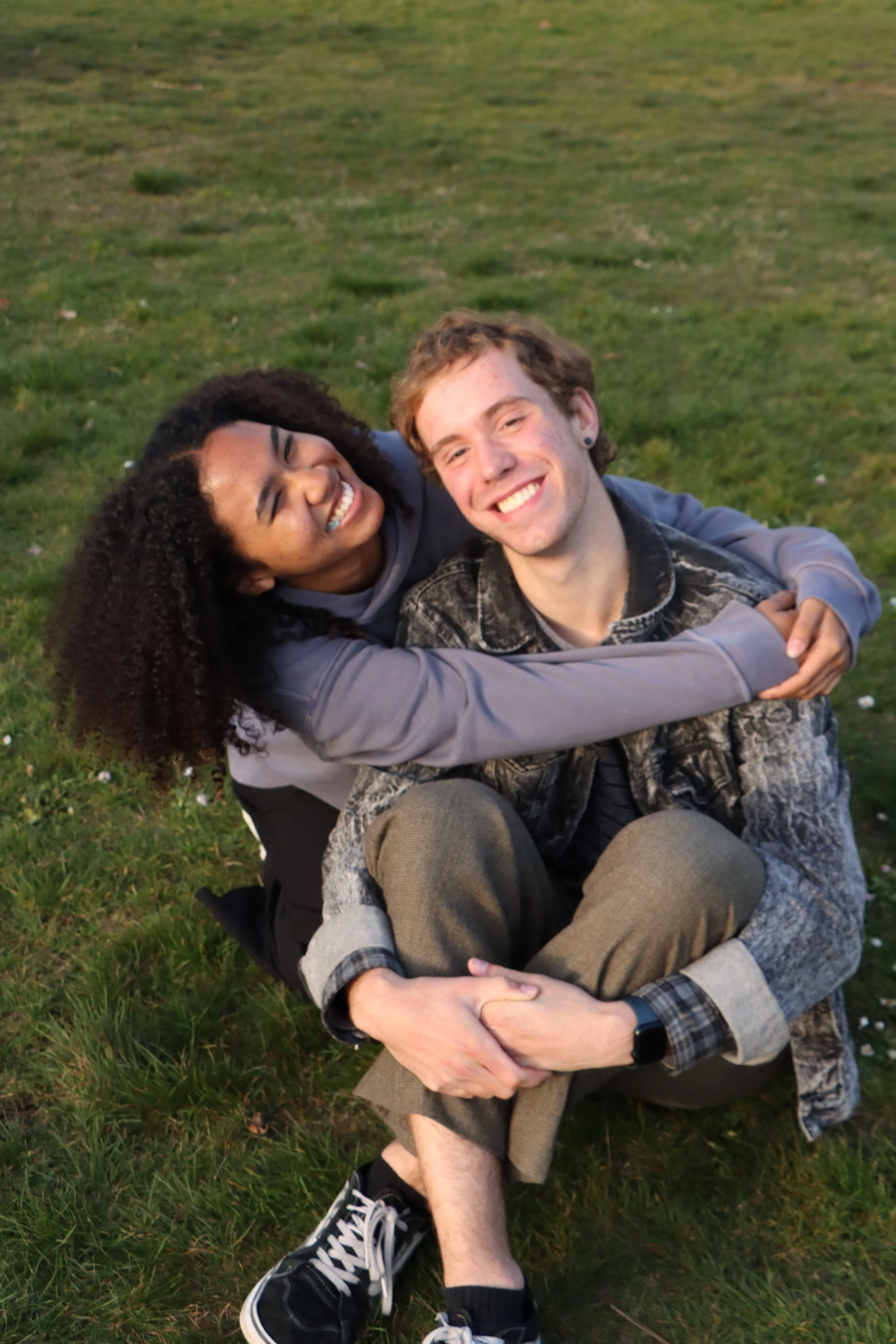 Two young people hugging on a grassy field, smiling and enjoying each other's company.