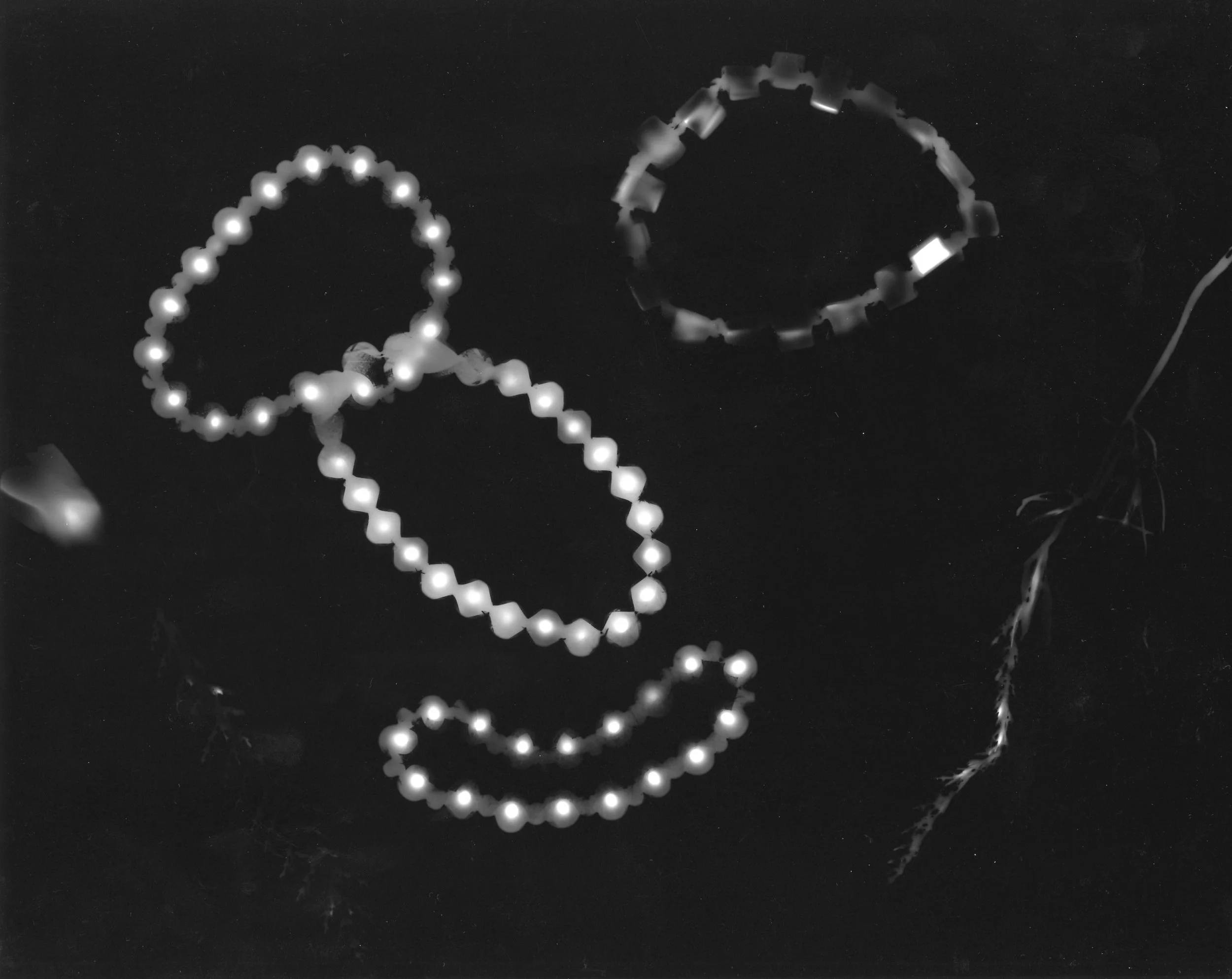 Glow-in-the-dark jewelry including beaded necklaces and a bracelet on a dark surface.