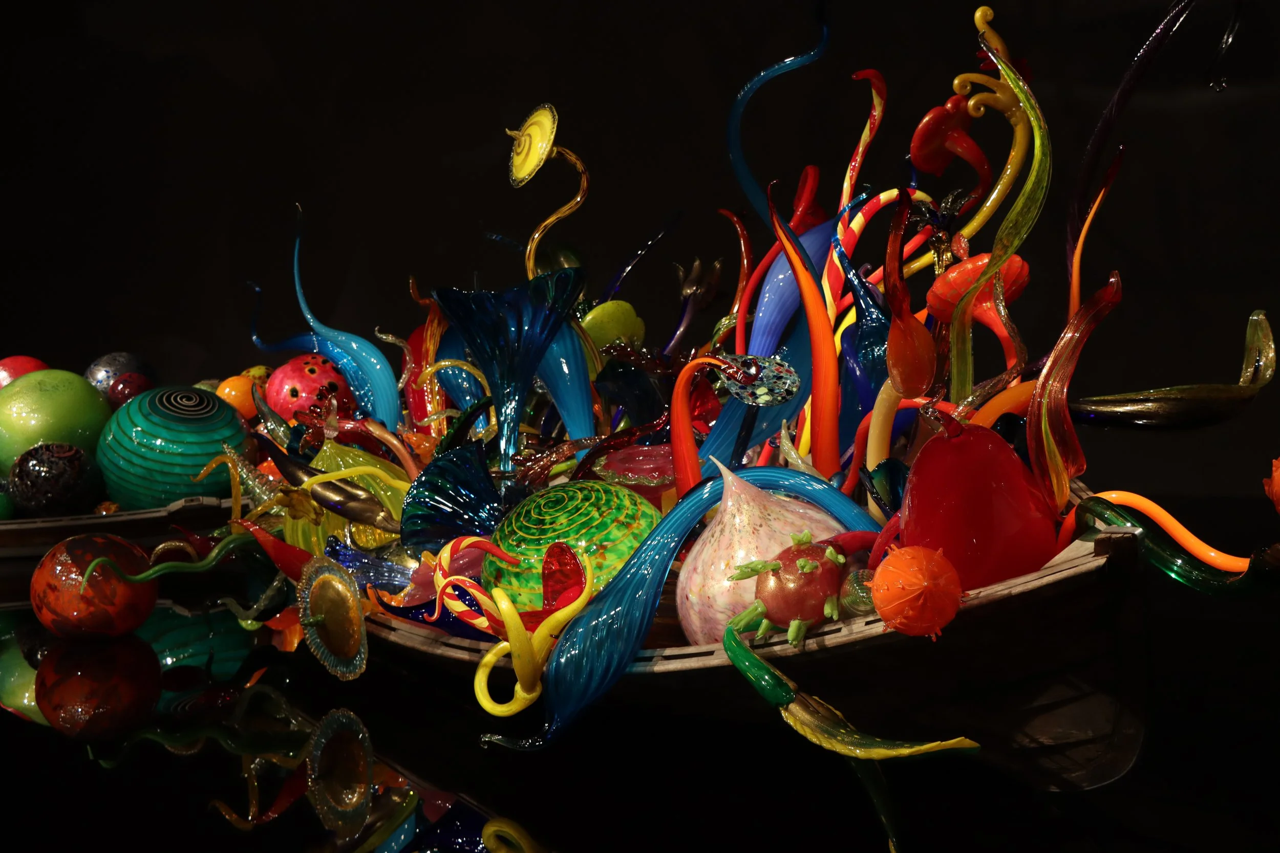 Colorful glass art sculptures on a black background, resembling sea creatures and abstract forms.