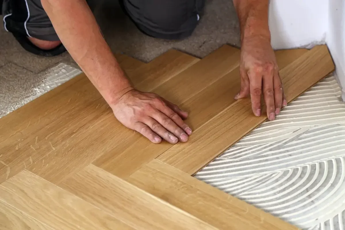 A person installing hardwood flooring, kneeling on the floor, aligning wooden planks.