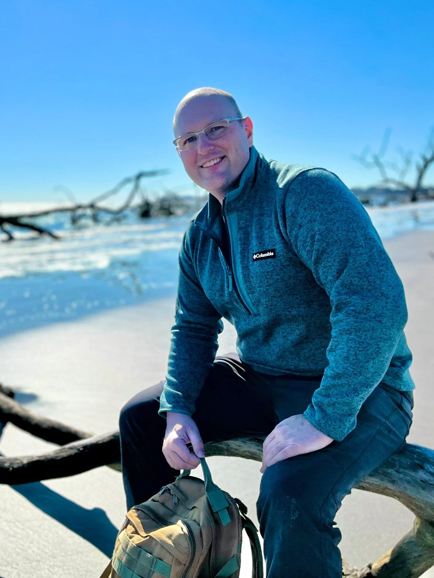 Man sitting on driftwood on a sunny beach by the ocean