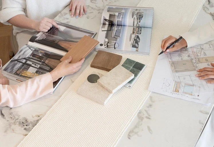 People examining architectural blueprints, samples, and images of furniture and interior design on a marble table.