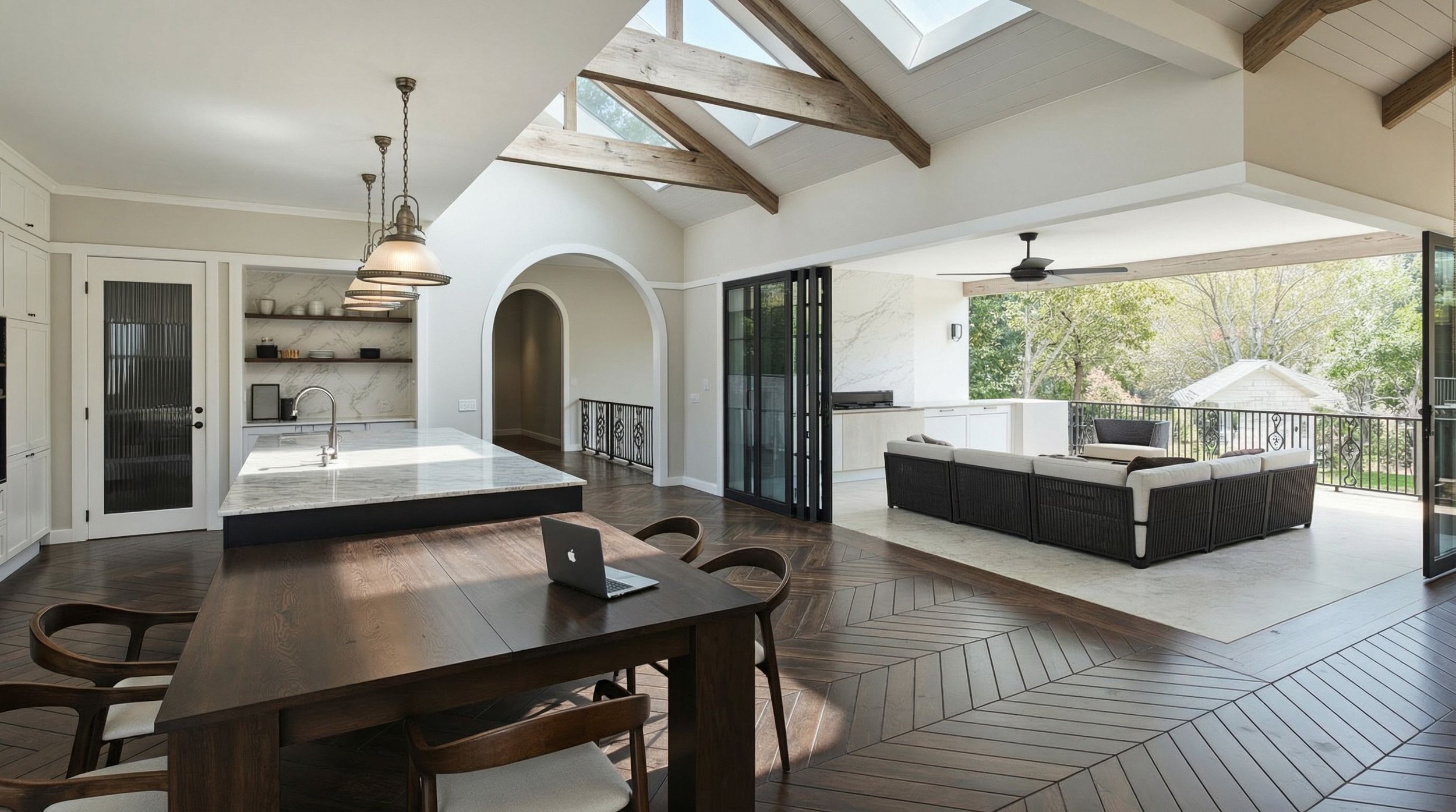 Modern open-concept living room and kitchen with large windows, skylights, white walls, dark wood flooring, and black outdoor furniture.