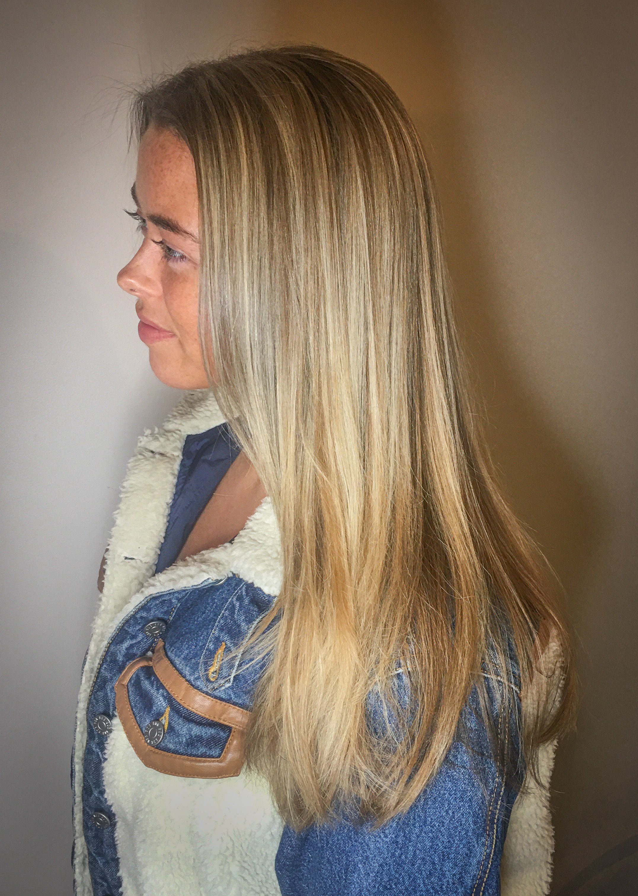 Profile of a woman with long, straight, blonde hair wearing a denim jacket with sherpa collar.