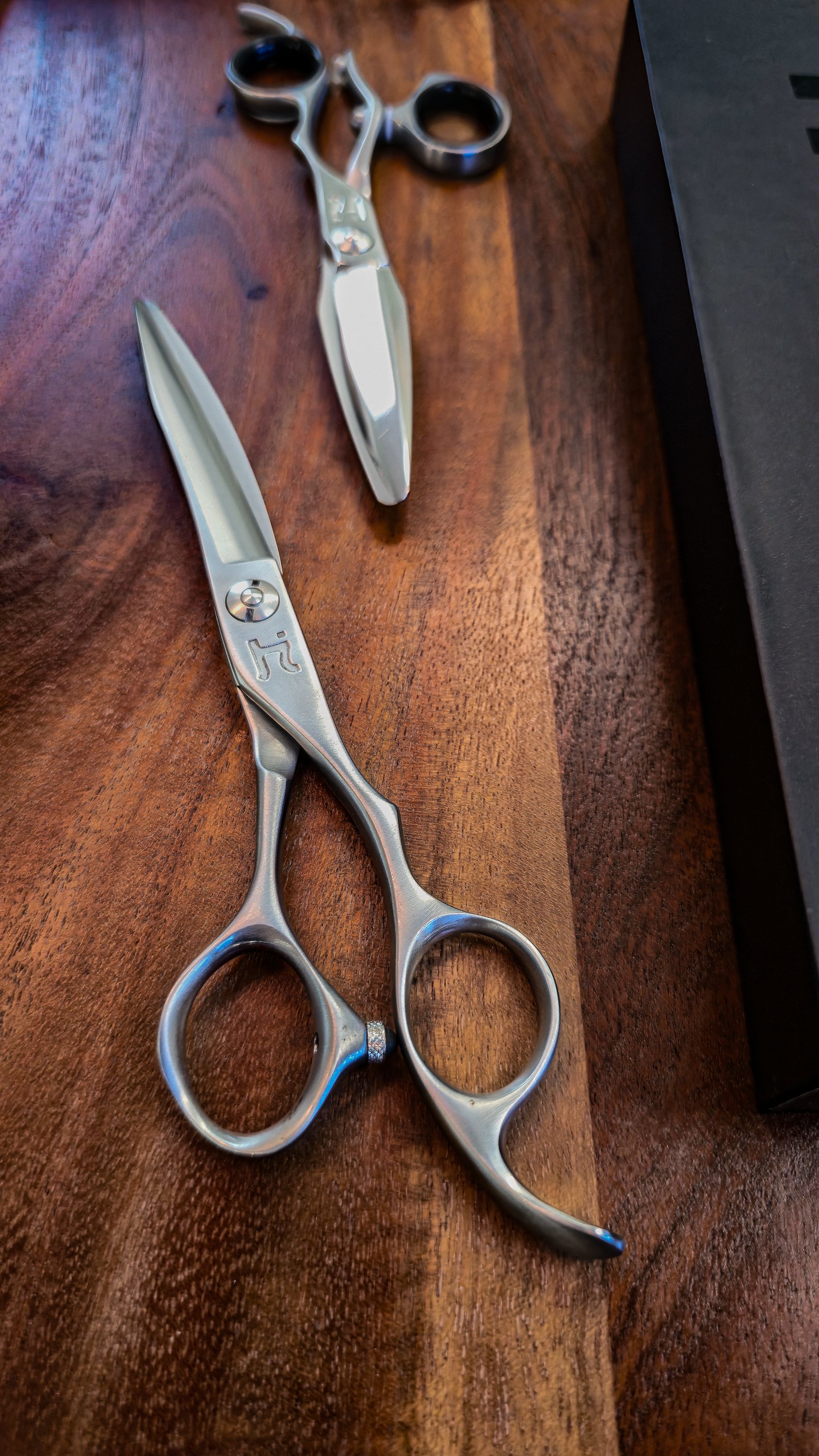 A pair of Hanzo professional hair scissors with a sleek silver finish placed on a wooden surface.