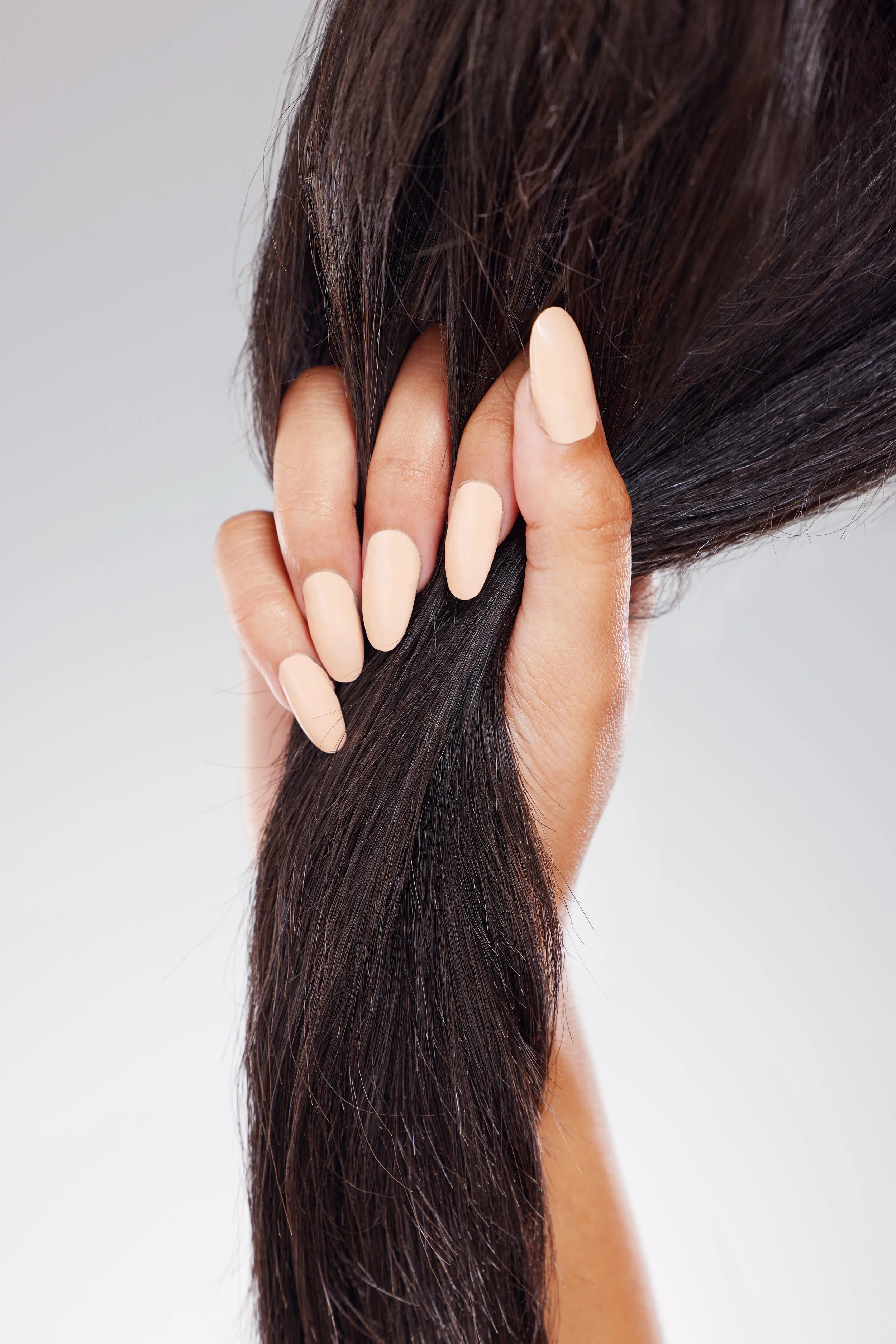 A person's hand with cream-colored polished nails holding a lock of long, dark brown hair.