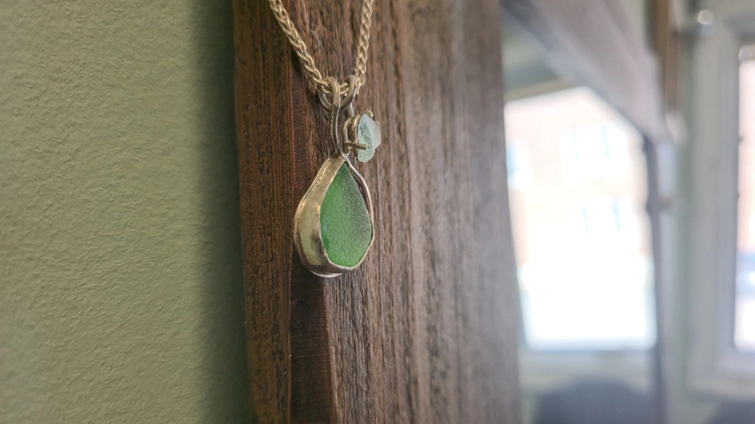 Silver necklace with a green teardrop-shaped pendant hanging on a wooden surface.