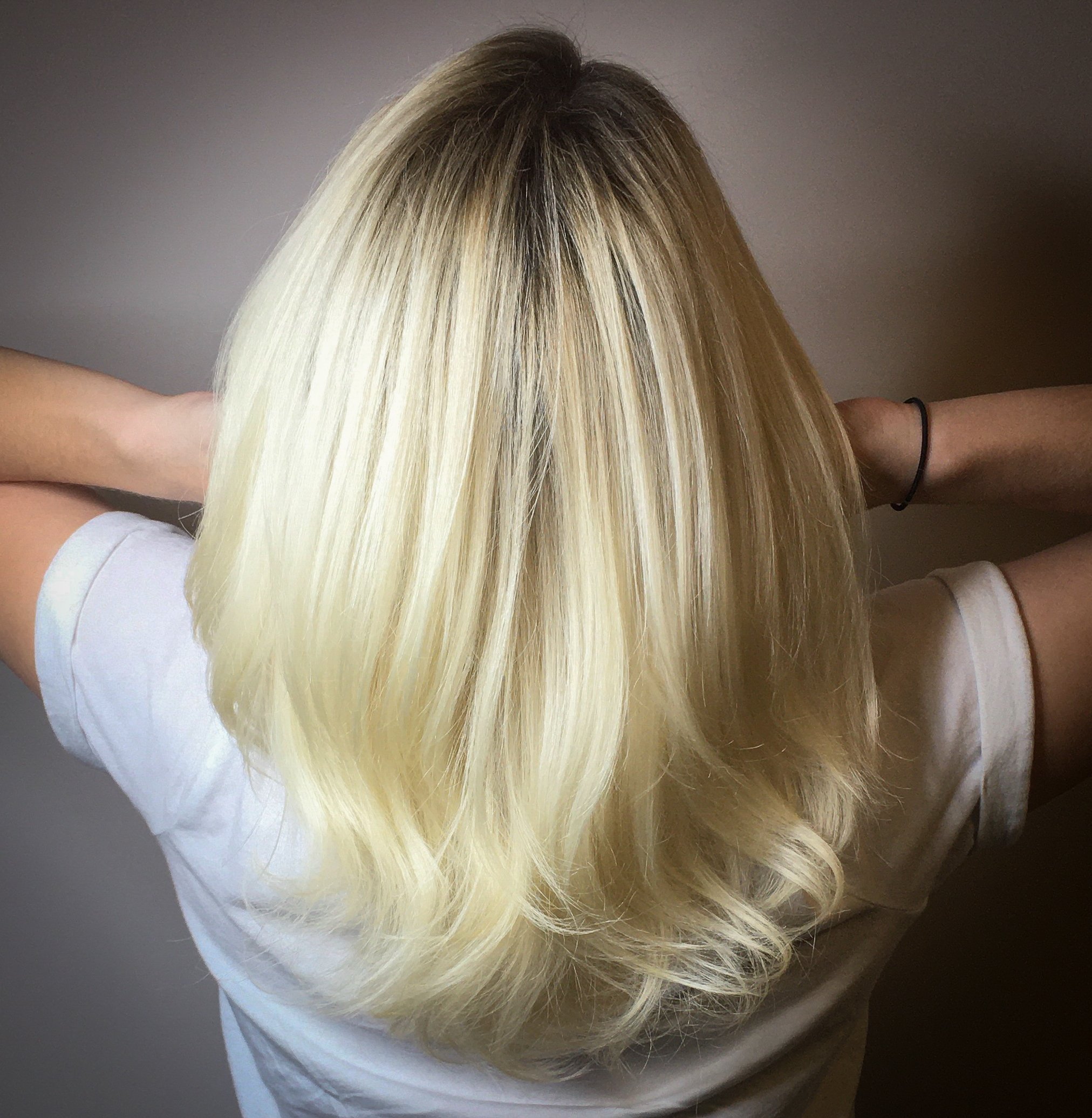 Person with long luminous blonde hair, wearing a white shirt, with arms raised and hands behind head showing off her new color.