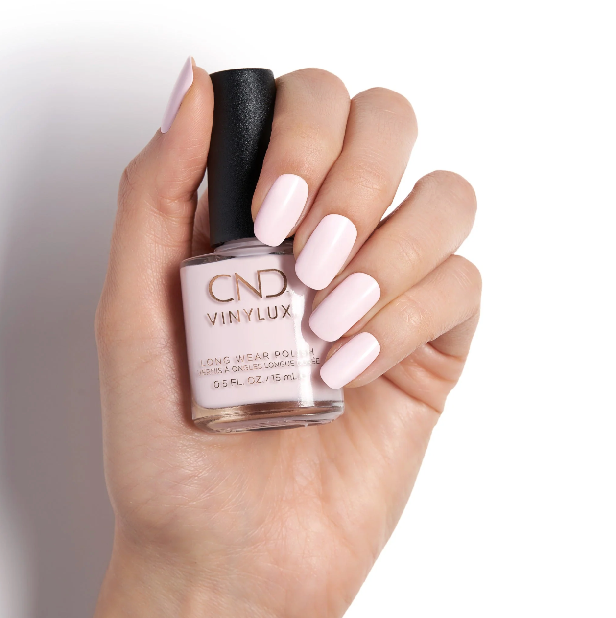 Close-up of a hand with manicured nails holding a bottle of pink nail polish against a white background.