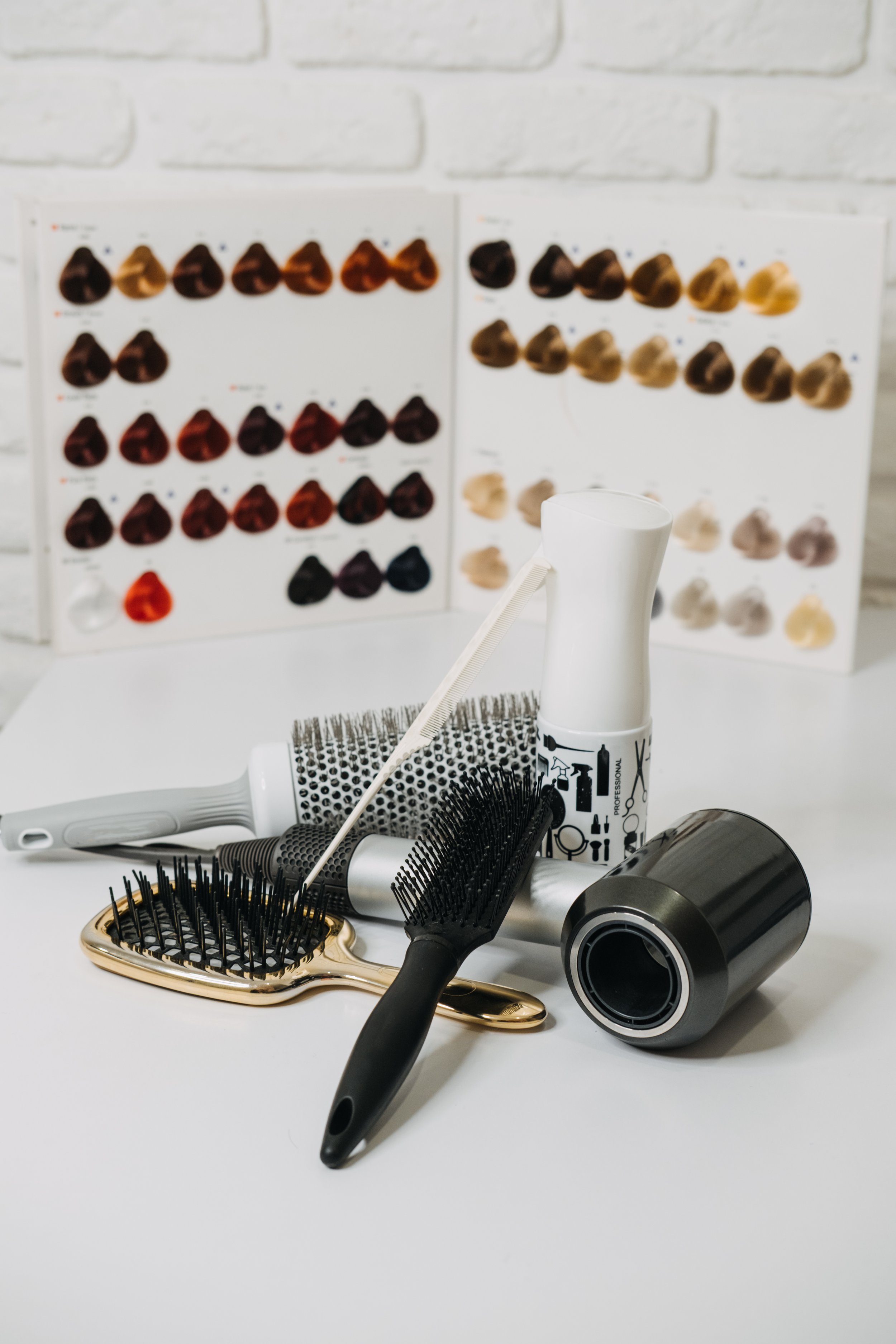 Hair styling tools including brushes, a round curling iron, and a spray bottle, with hair color chart samples in the background.