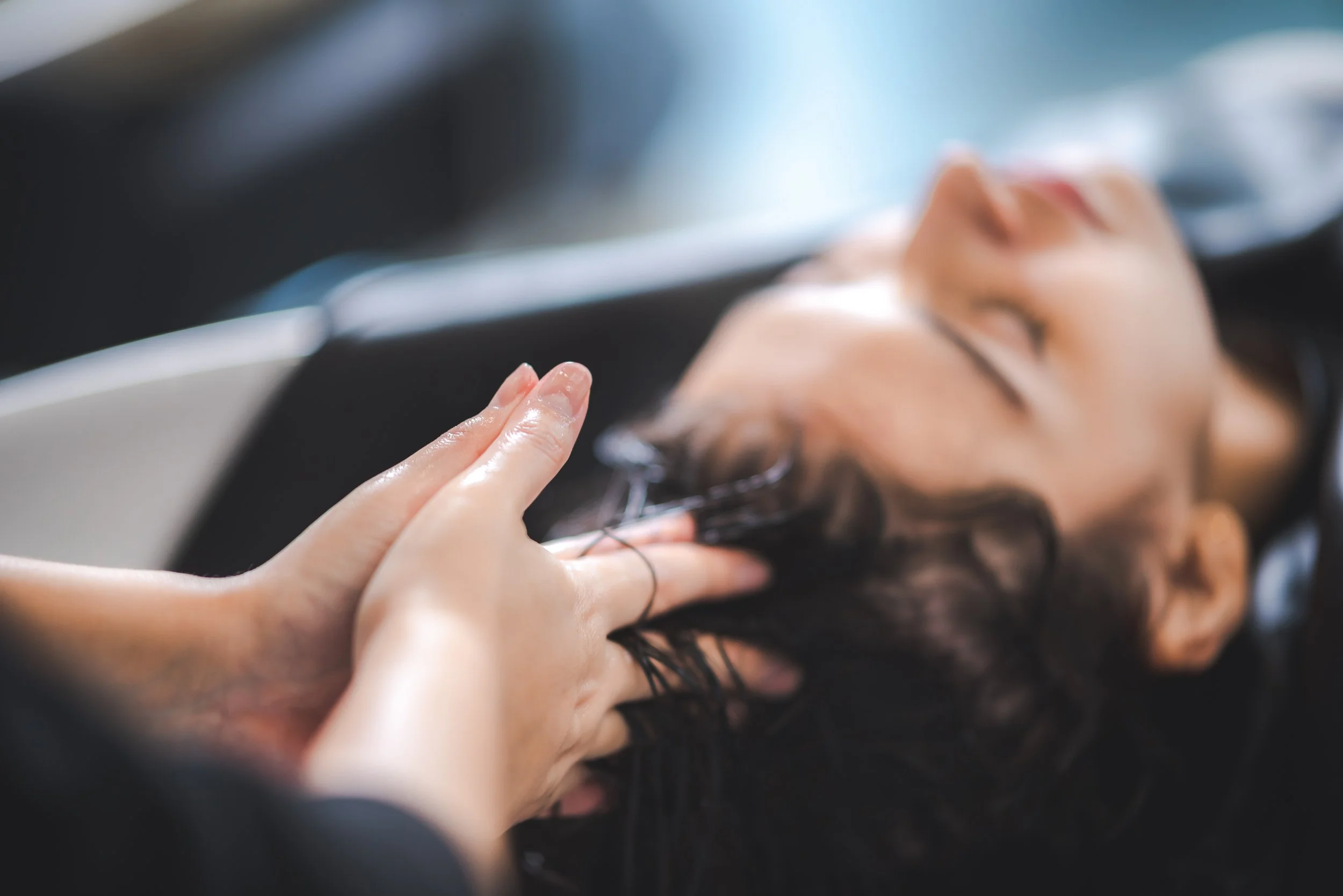 A woman receiving a relaxing shampoo and blowout hair treatment at a salon, lying with eyes closed.