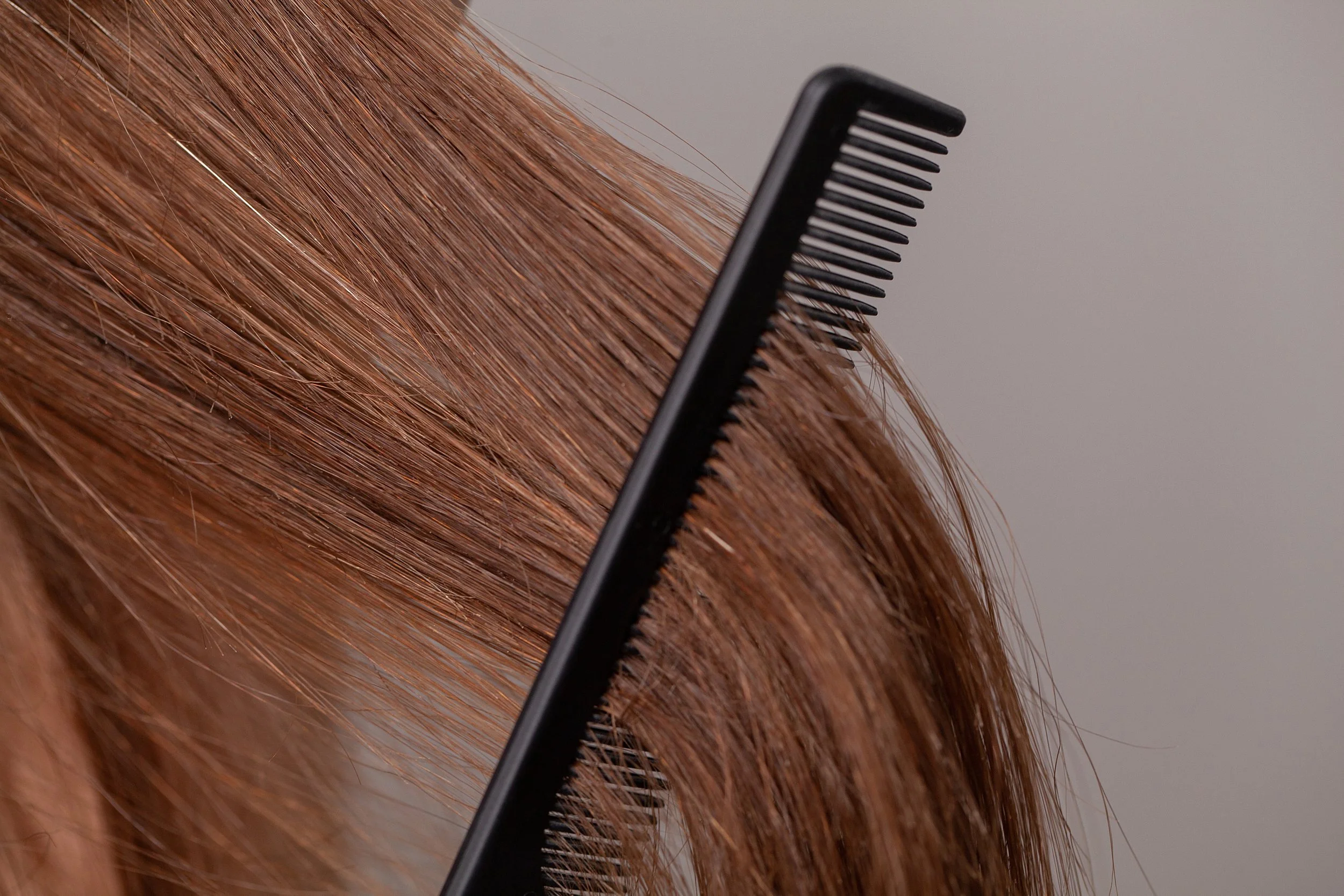 Close-up of a black hair comb running through straight, reddish-brown hair on a person.