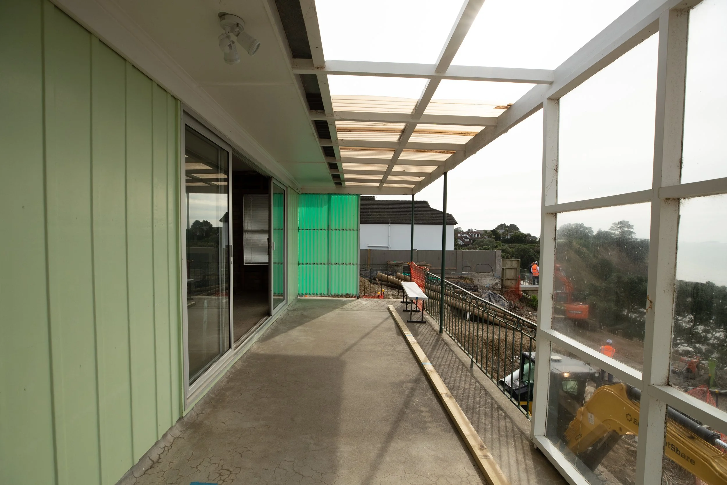 Under construction balcony with glass sliding doors on the left and a partially built white railing on the right. Construction workers and equipment are visible in the background.